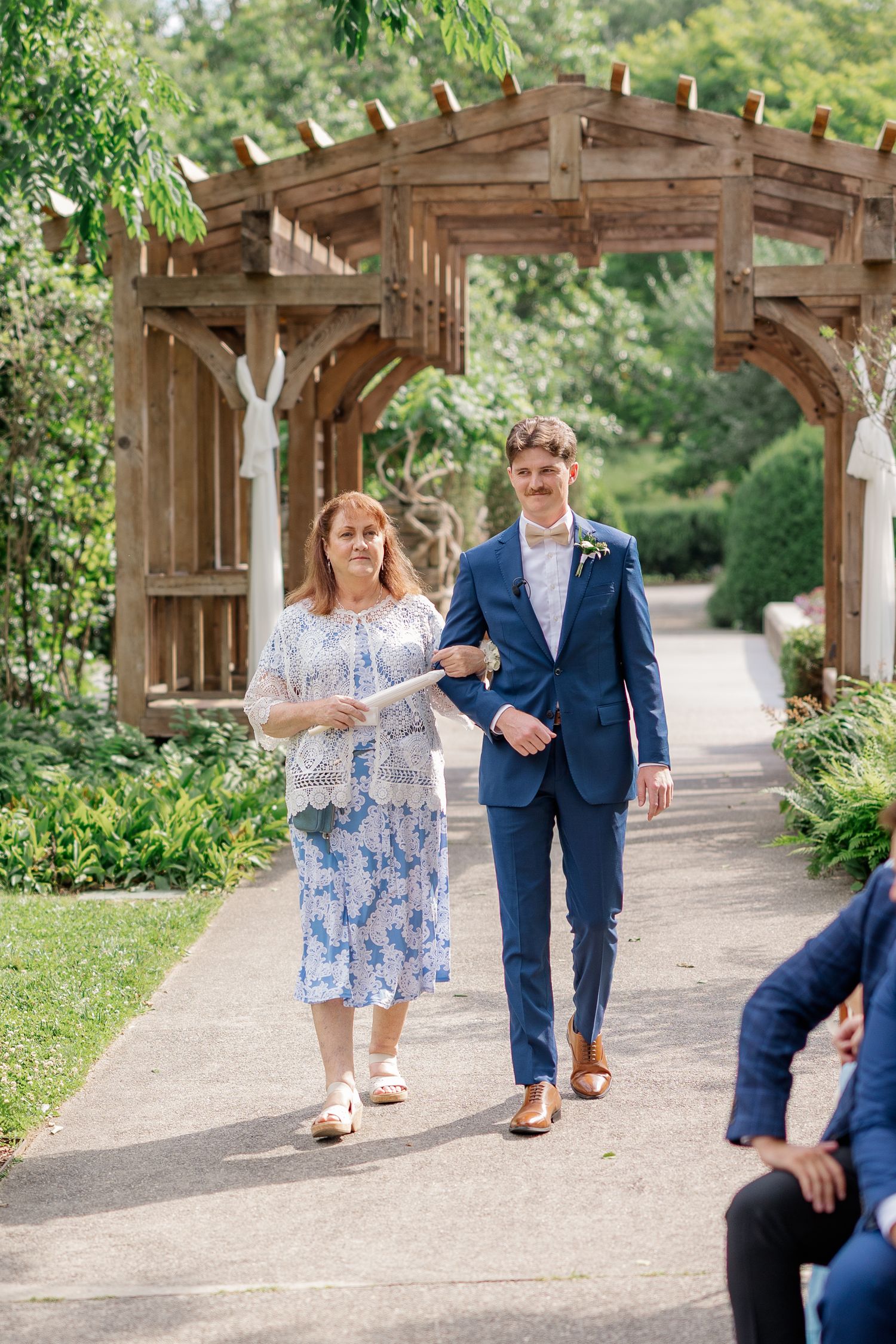 Wedding couple walking and posing under wooden garden pergola surrounded by greenery.