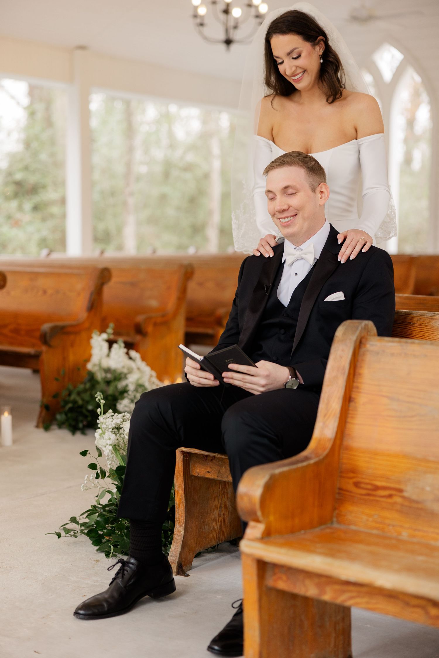 Wedding couple shares intimate moment on wooden church pews in bright sunlit chapel.