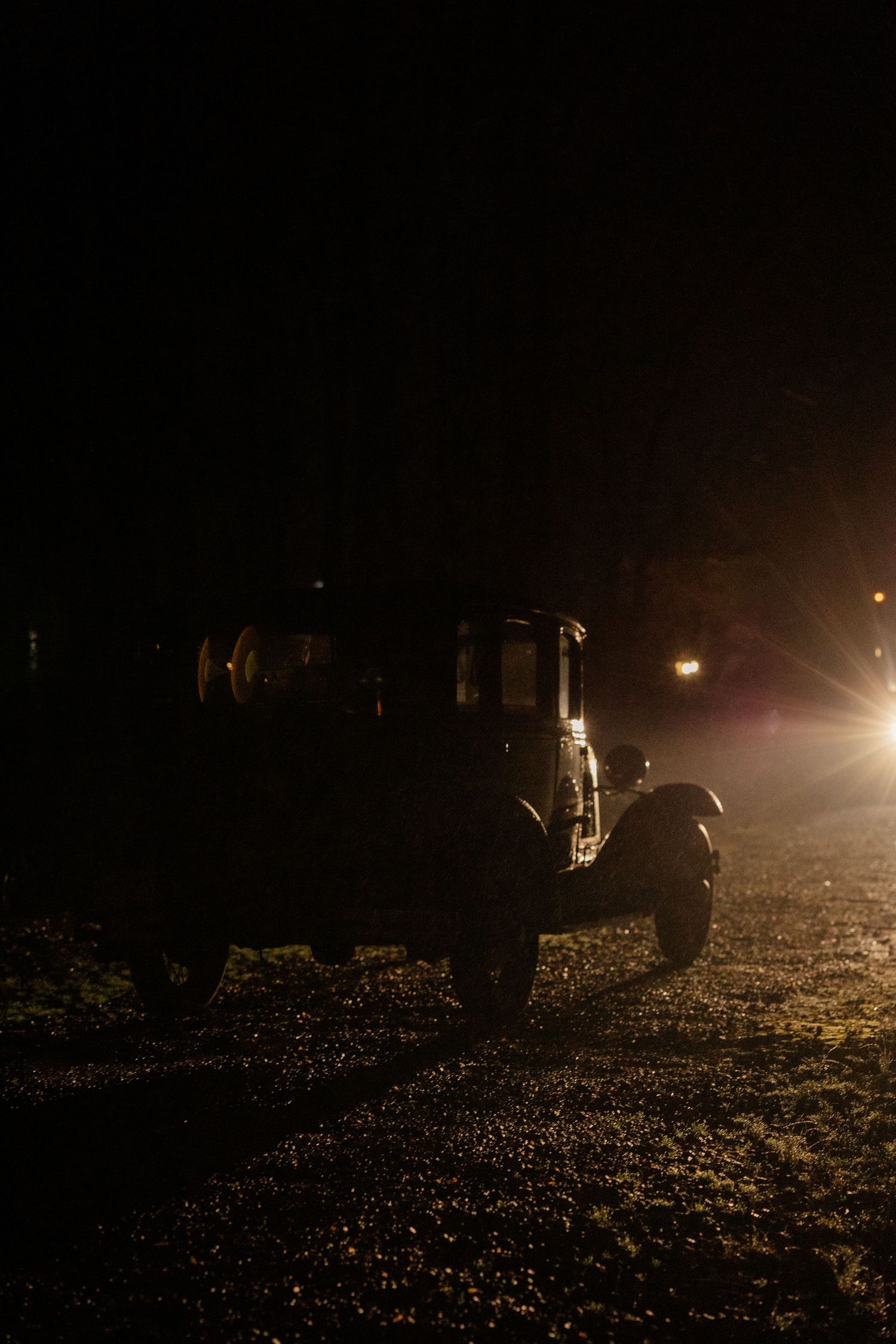 Dark silhouettes of vehicles illuminated by headlights in a nighttime parking area.