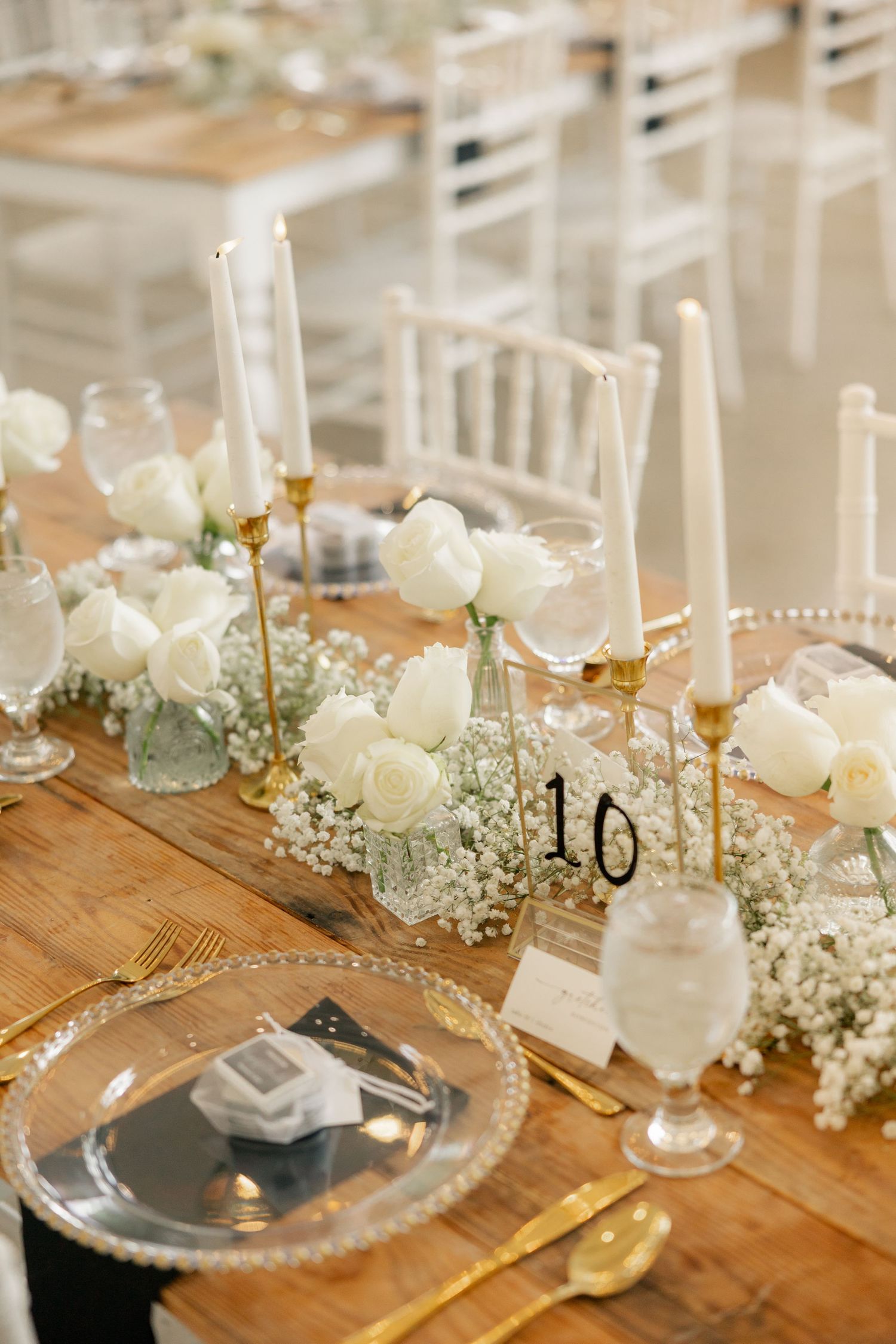 An elegant wedding reception table setting with white flowers, baby's breath, and gold accents.