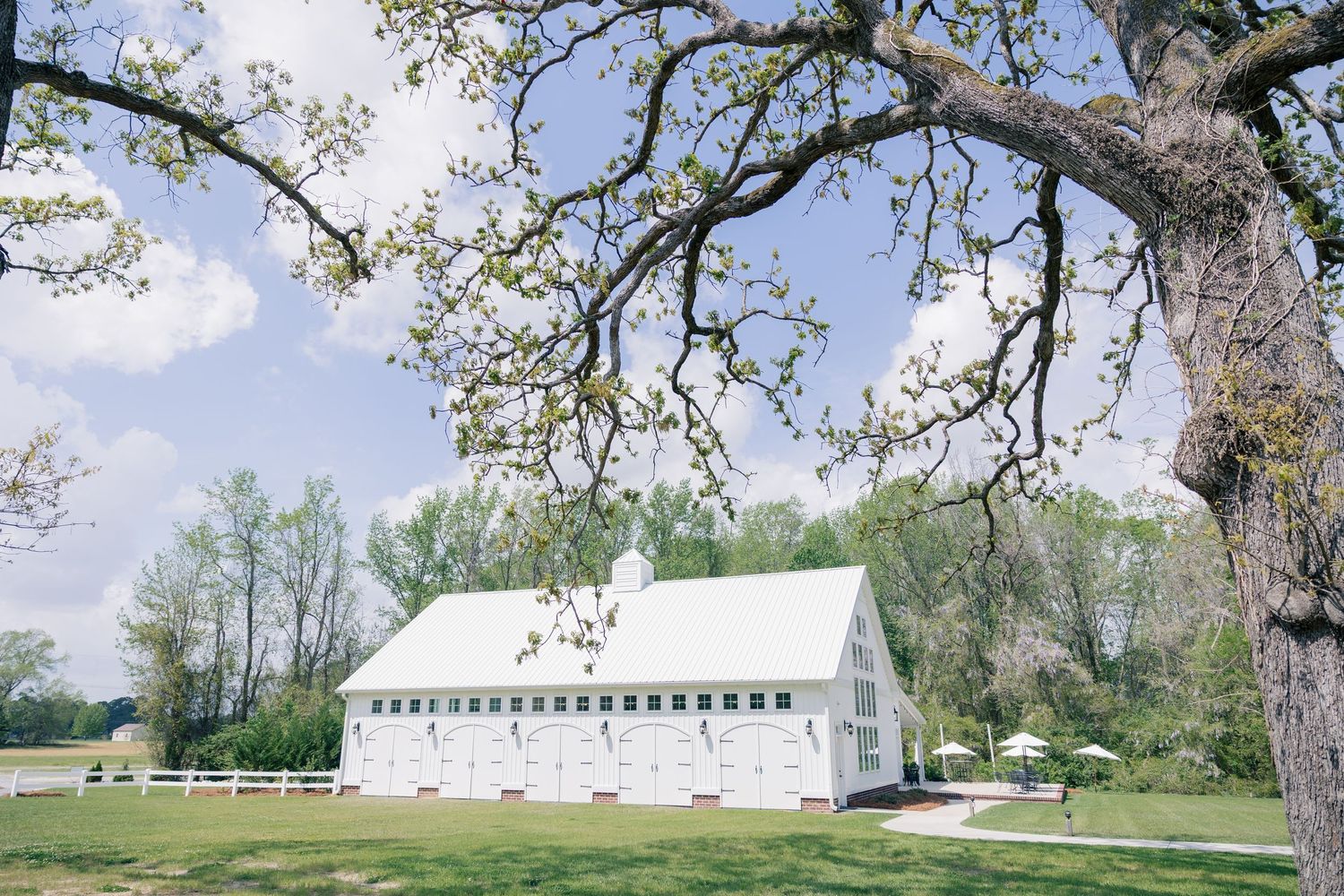 Panoramic view of a rustic white church building in a pastoral countryside setting with large trees.