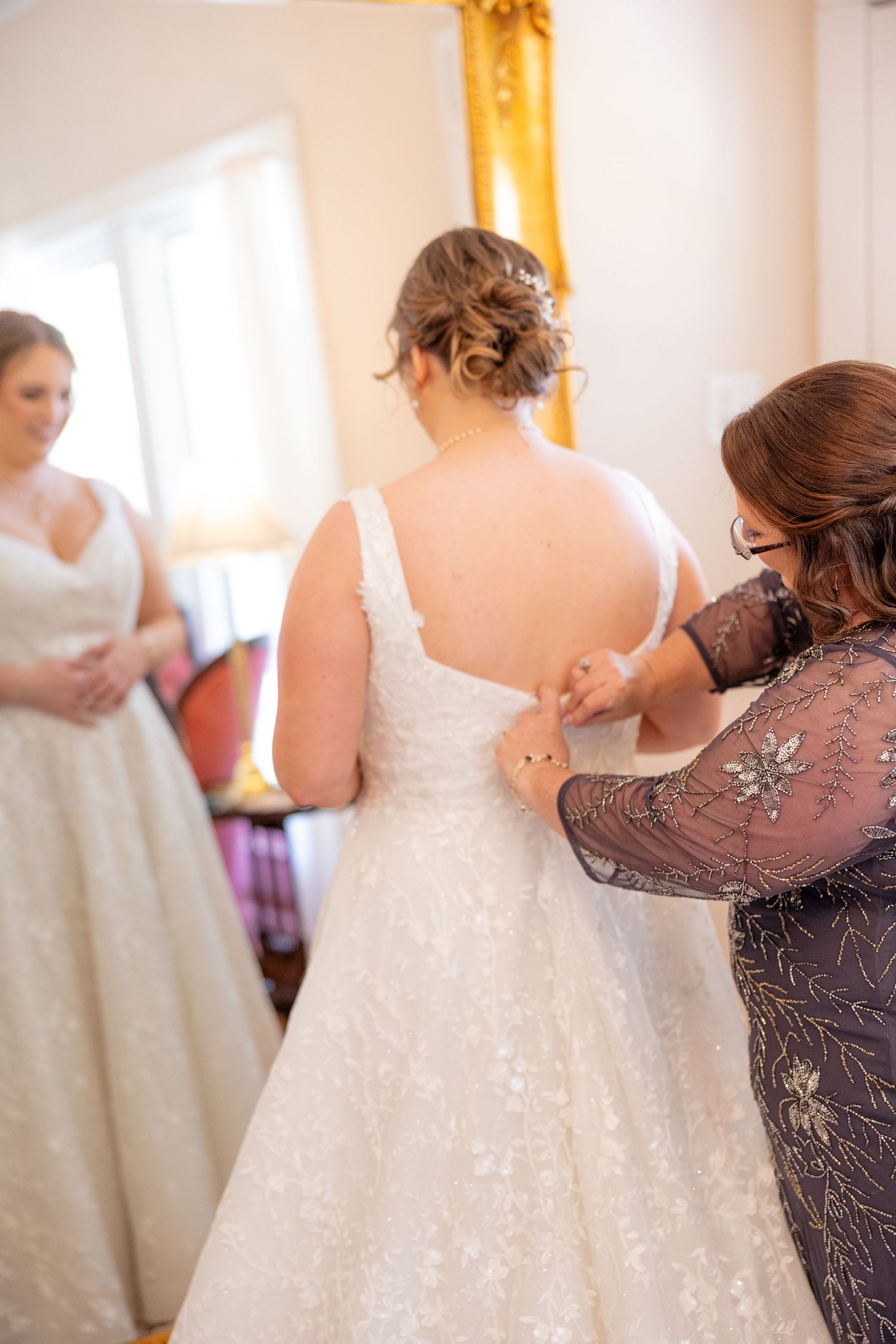Close up view of someone helping a bride get into an elegant white wedding dress with lace details.