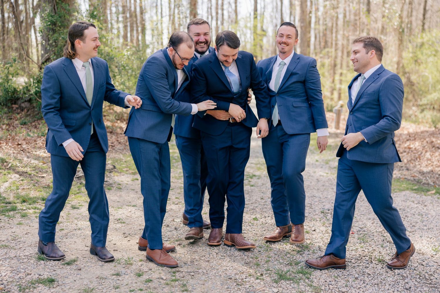 Groomsmen in navy suits huddle together looking at something on a phone, sharing a candid moment.