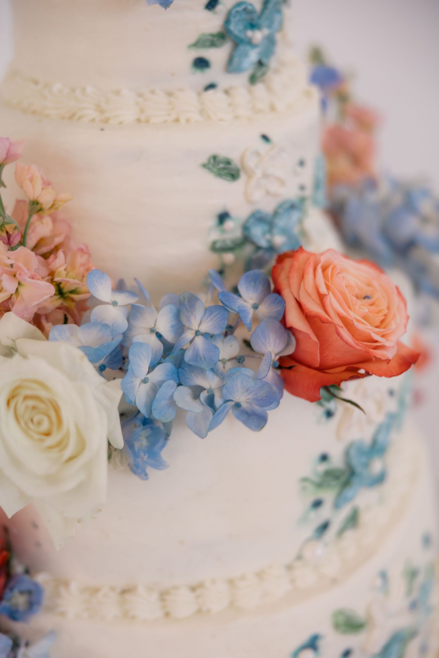 Wedding cake decorated with delicate blue hydrangeas, coral and white roses in a romantic design.