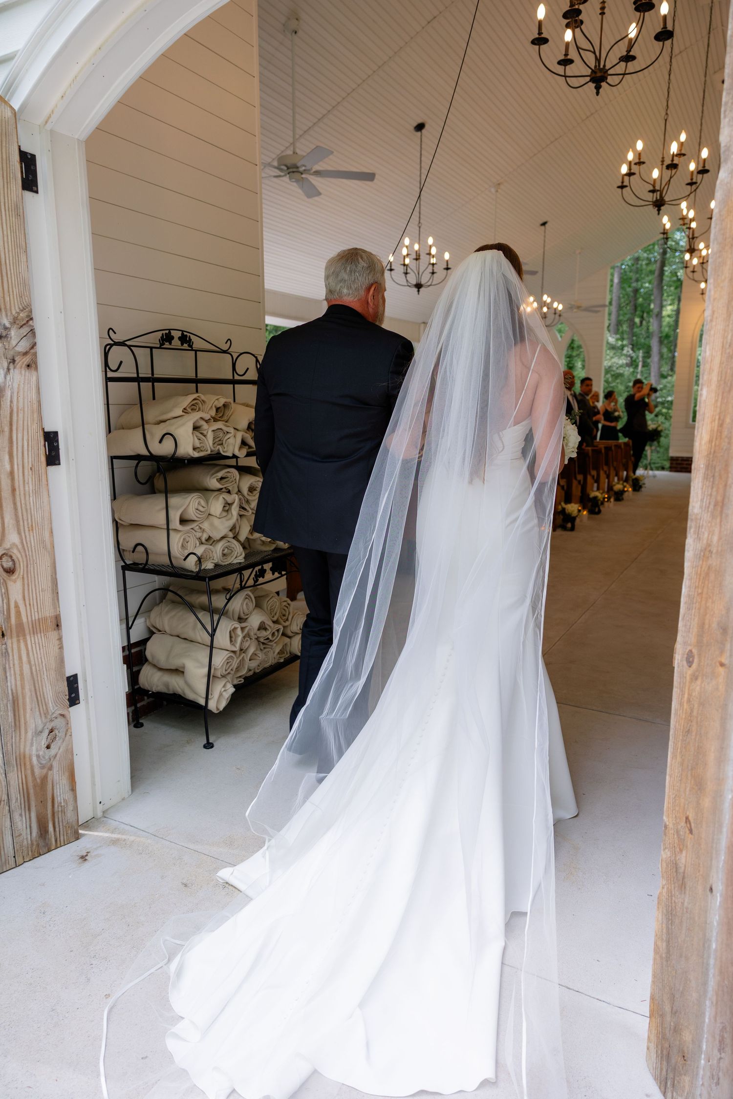Wedding venue interior with white draped fabric, wooden beams and elegant chandeliers.
