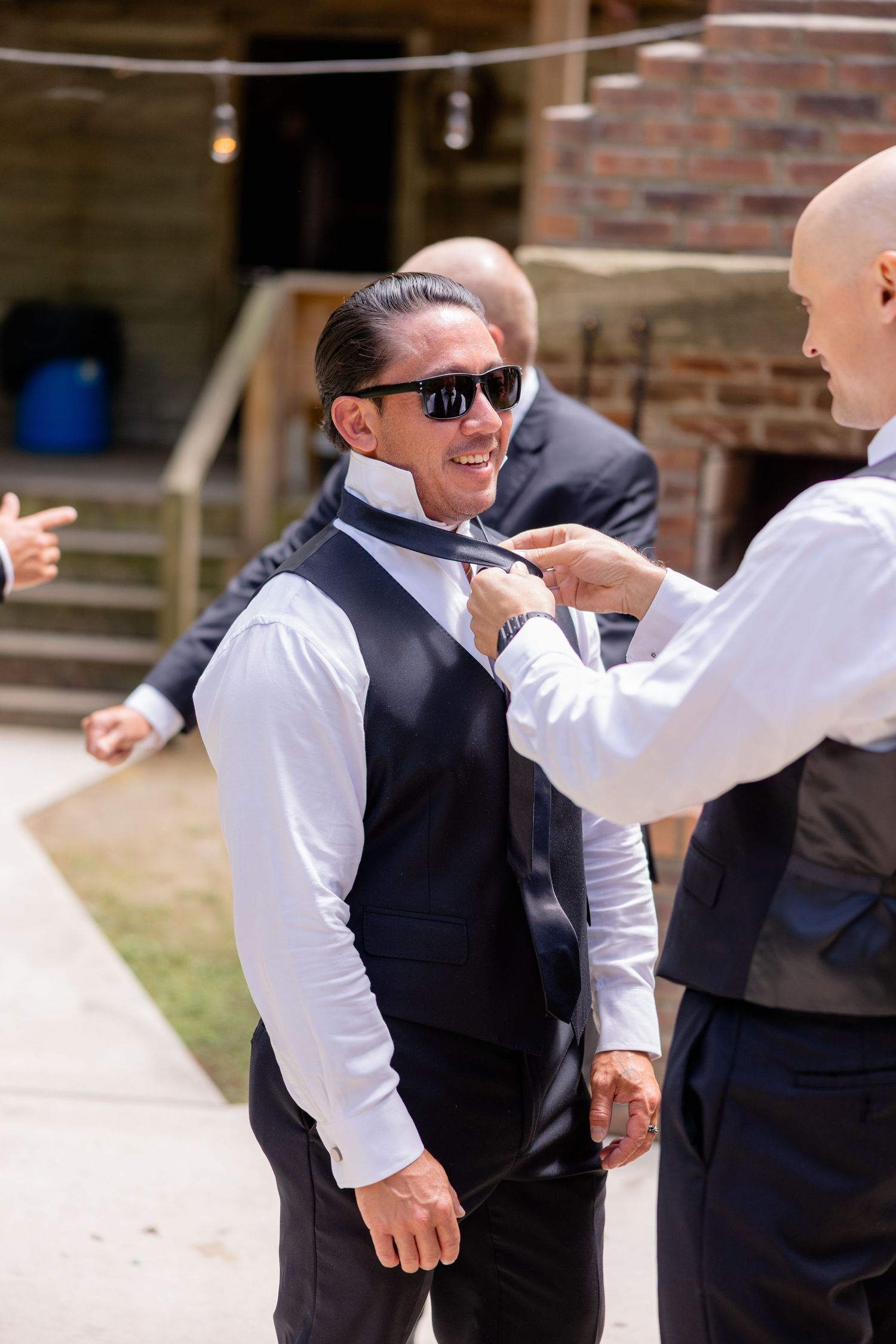 A formal dressing scene shows the final adjustments of a black vest and tie before a wedding ceremony.