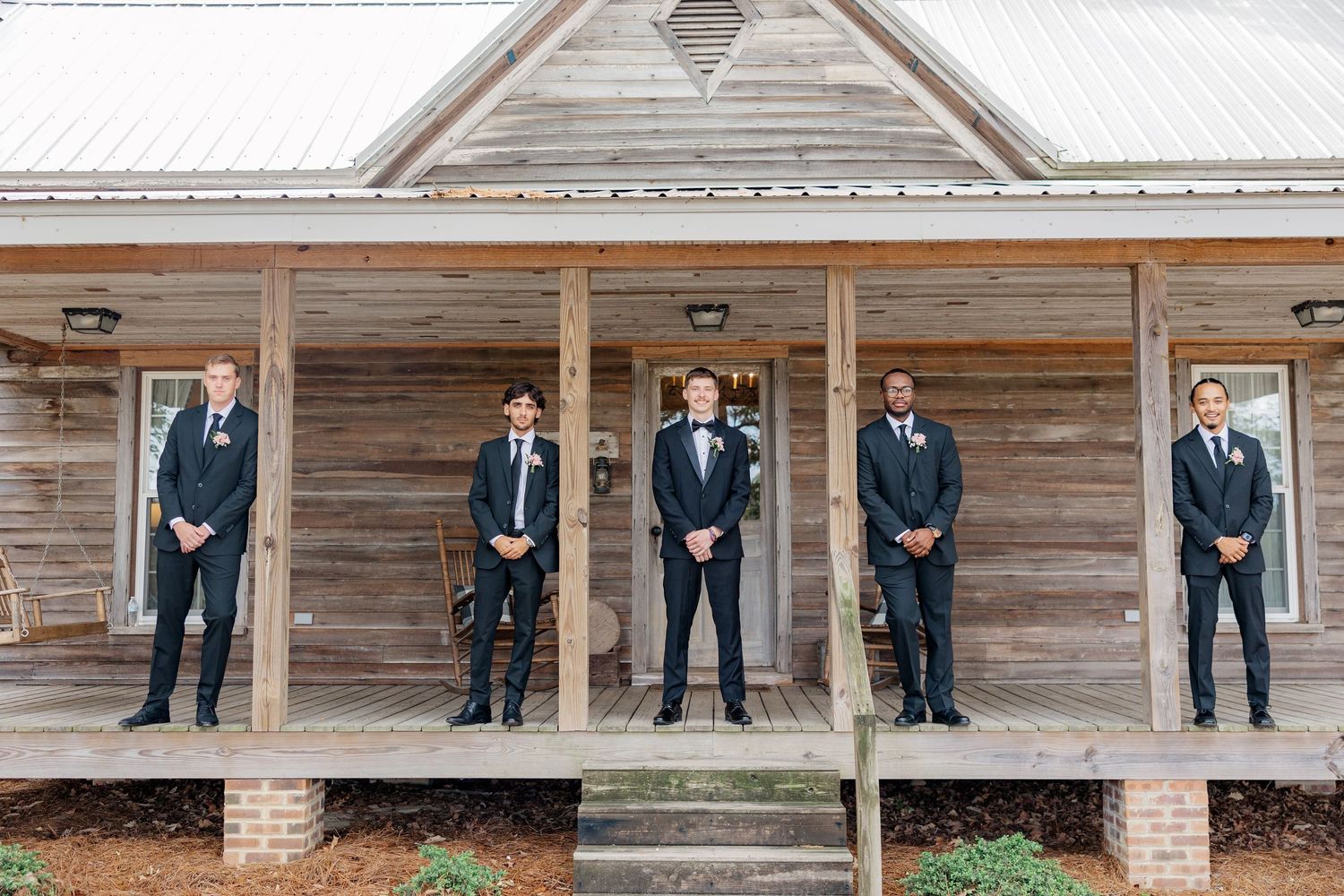 Groomsmen in navy suits standing in a line on the porch of a rustic wooden building.