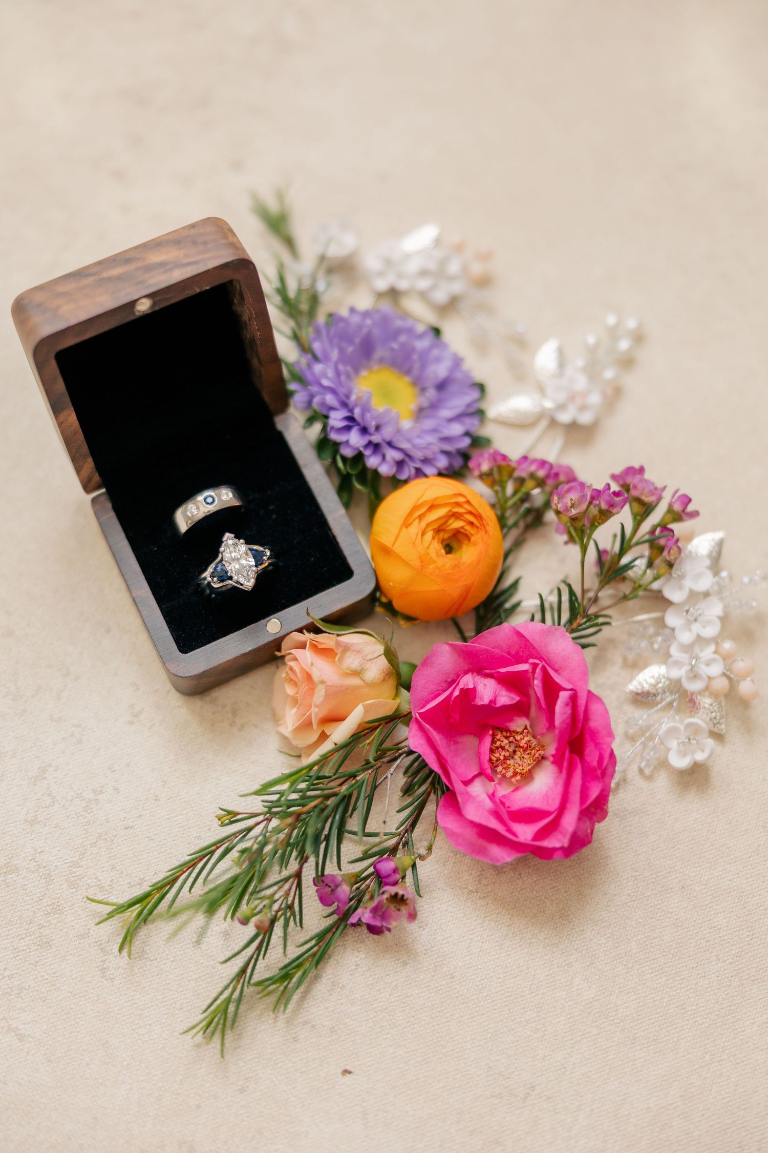 Diamond engagement ring in wooden box surrounded by colorful wildflowers including ranunculus and asters.