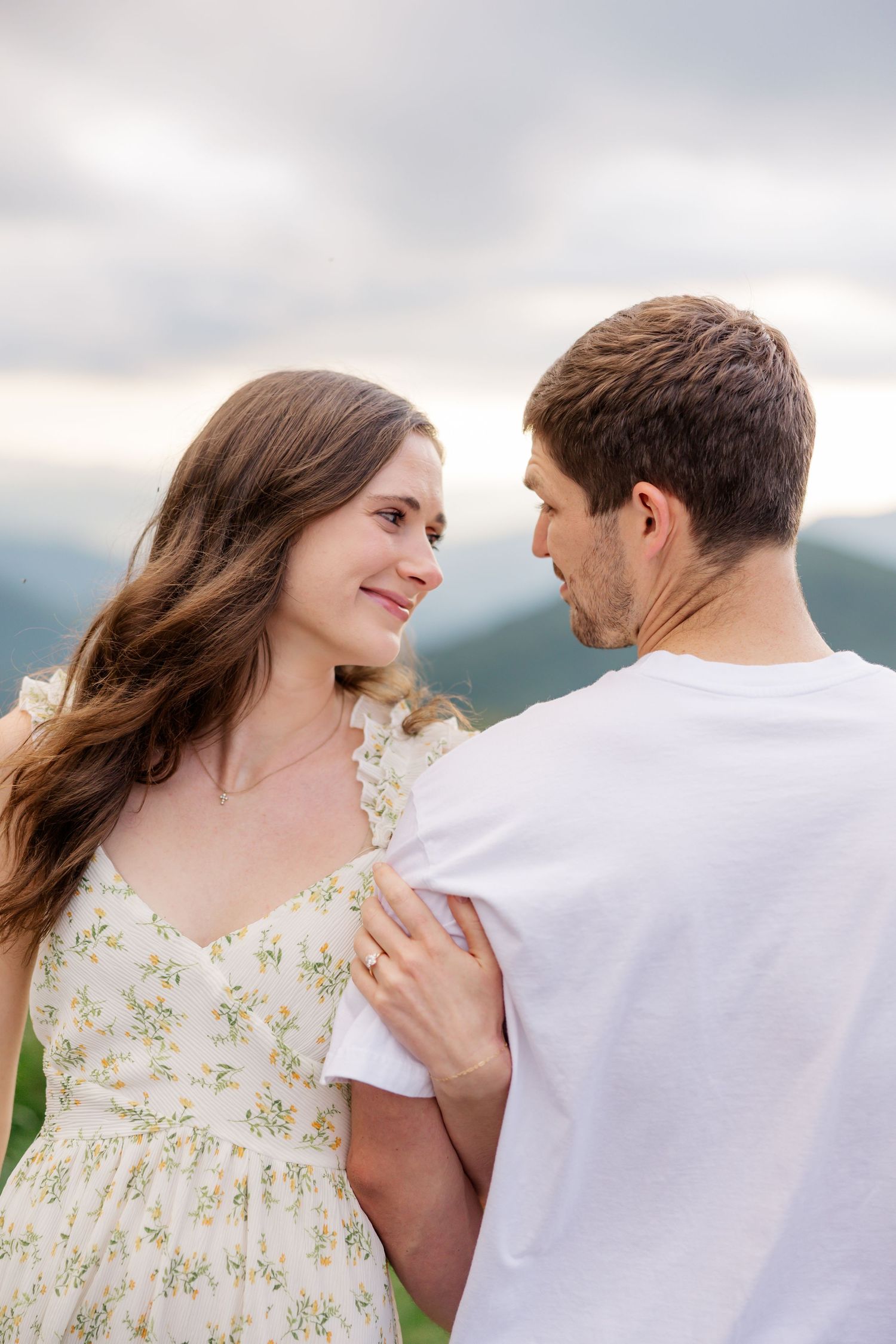 Couple in white dress and t-shirt sharing an intimate moment against a mountain landscape.