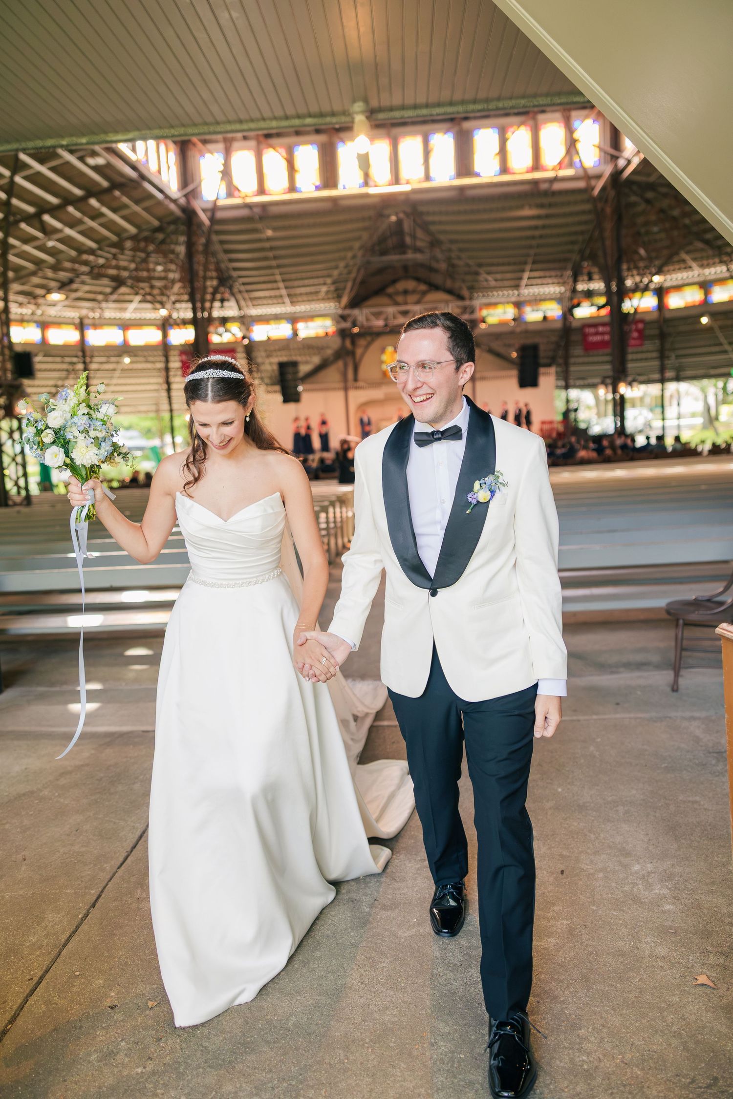 Joyful newlyweds walk hand in hand down the aisle after wedding ceremony in elegant pavilion venue.