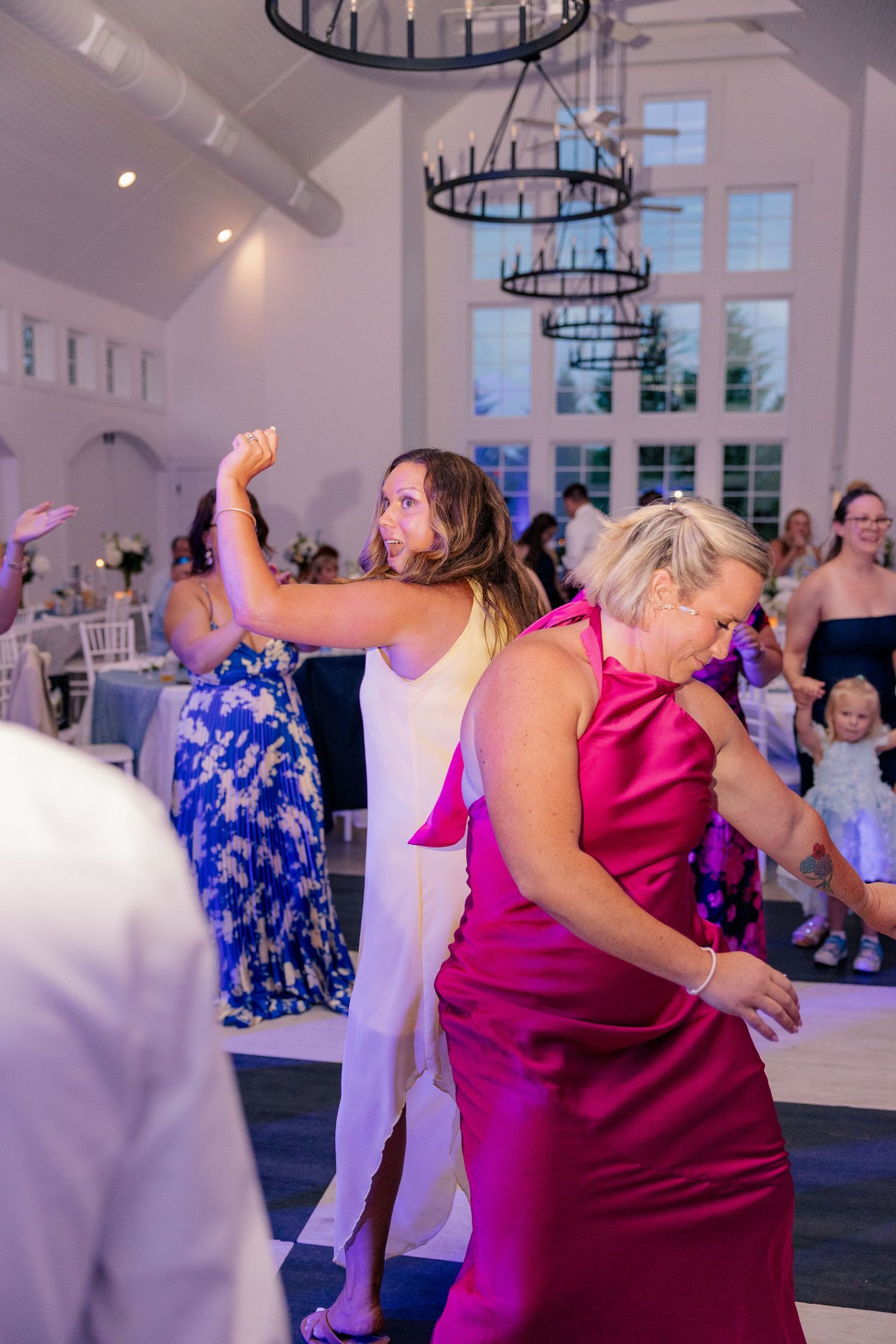 Guests dance energetically on wedding reception dance floor in bright white venue.