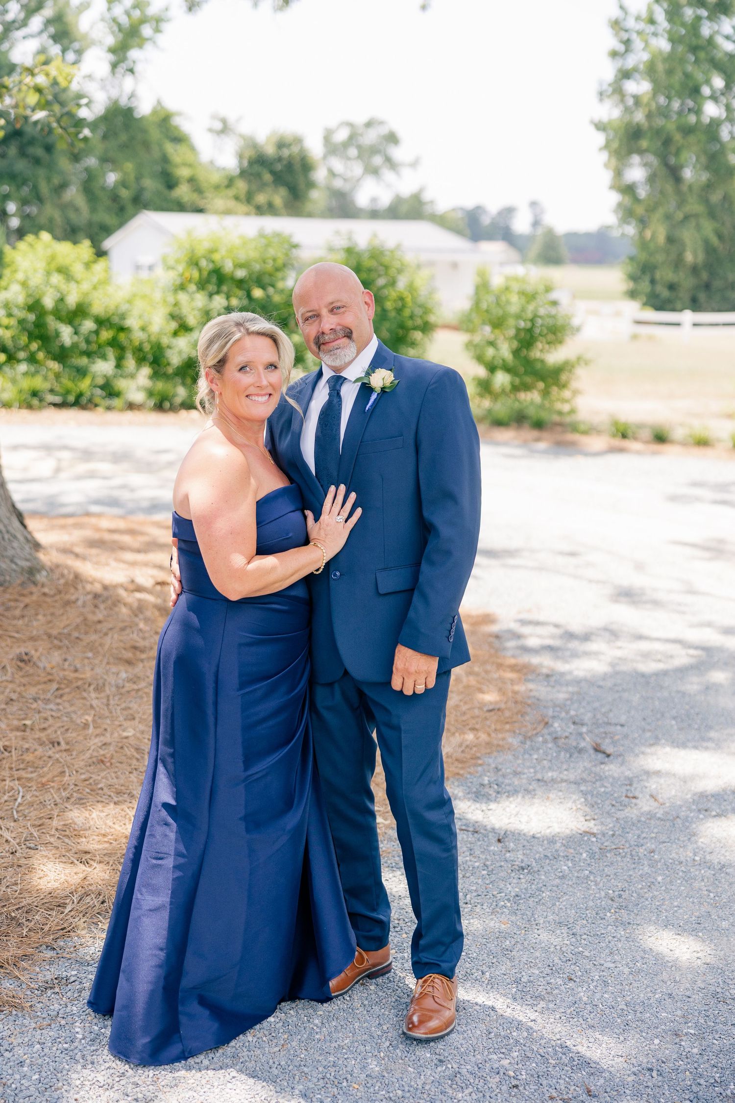 Couple in matching navy blue formal attire posing outdoors at wedding venue.