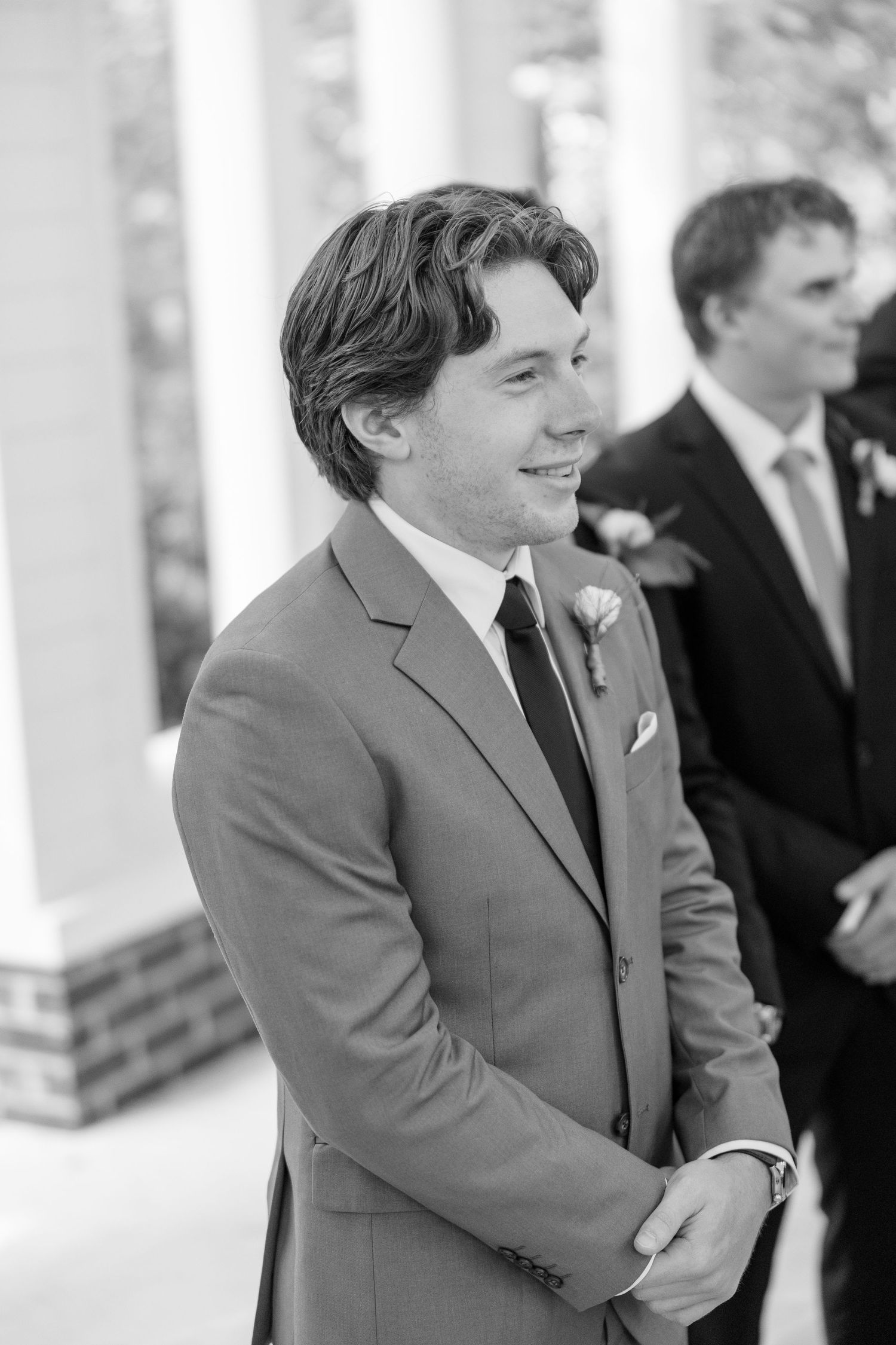 Black and white portrait of smiling groom in gray suit at outdoor ceremony.