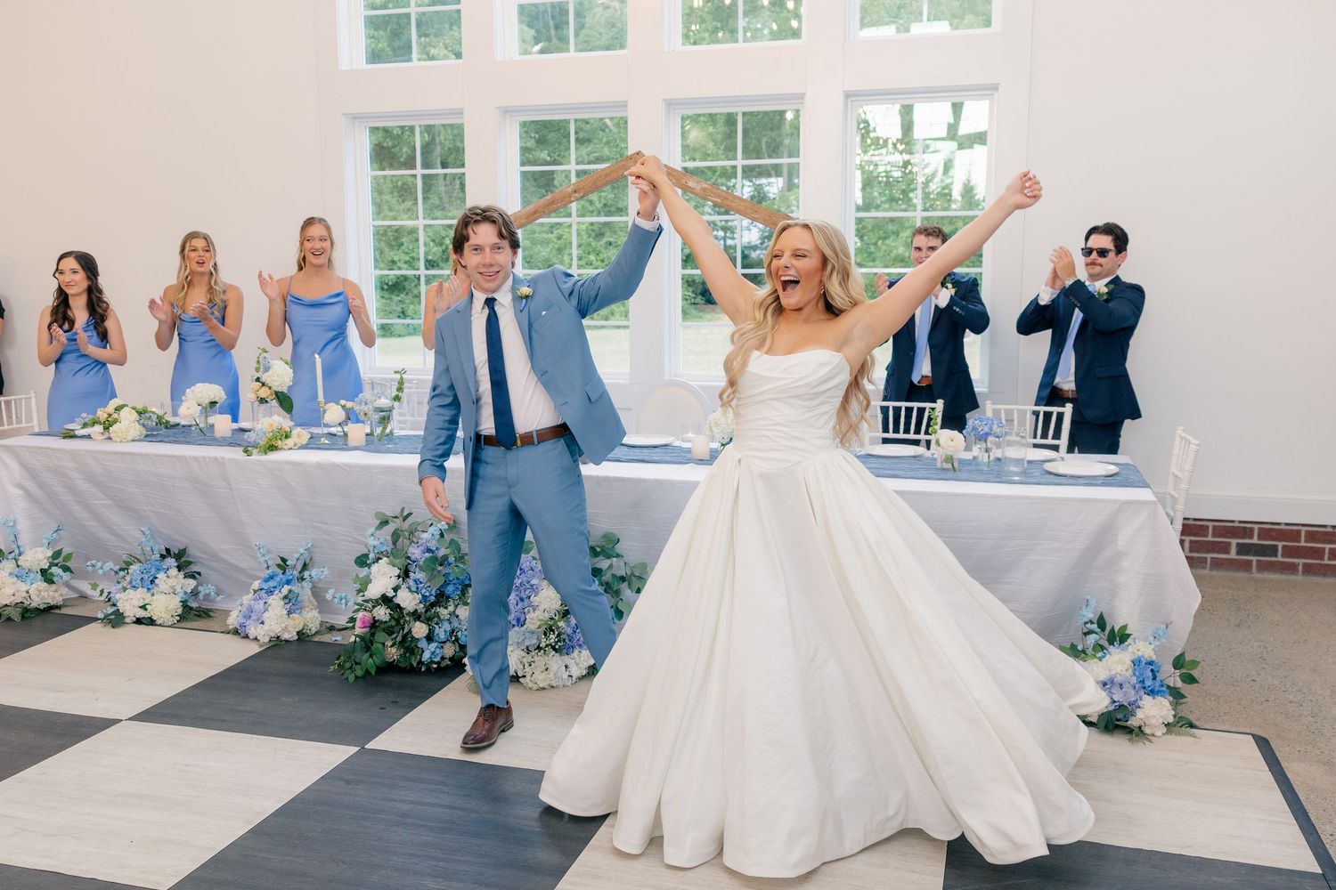 Bride and groom enter reception hall triumphantly with bridesmaids in blue.