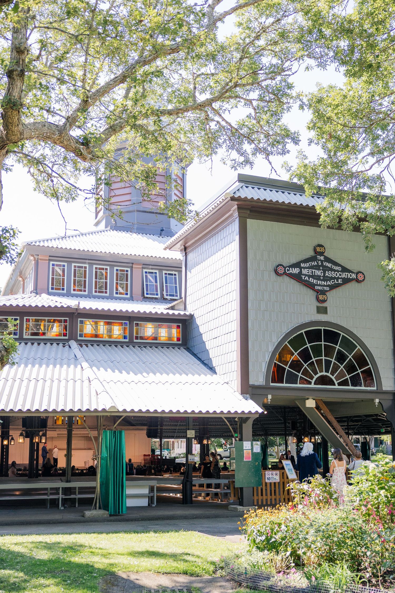 Historic Camp Meeting Association building with covered outdoor dining area surrounded by lush trees on a sunny day.