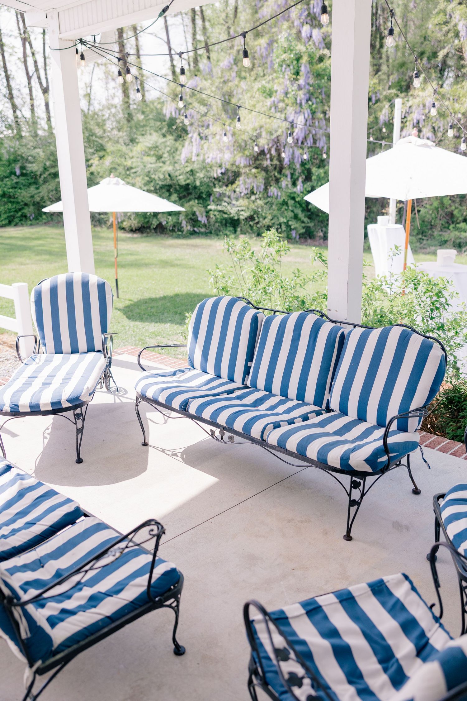 Outdoor porch with striped blue and white cushioned benches arranged along white columns in a peaceful garden setting.
