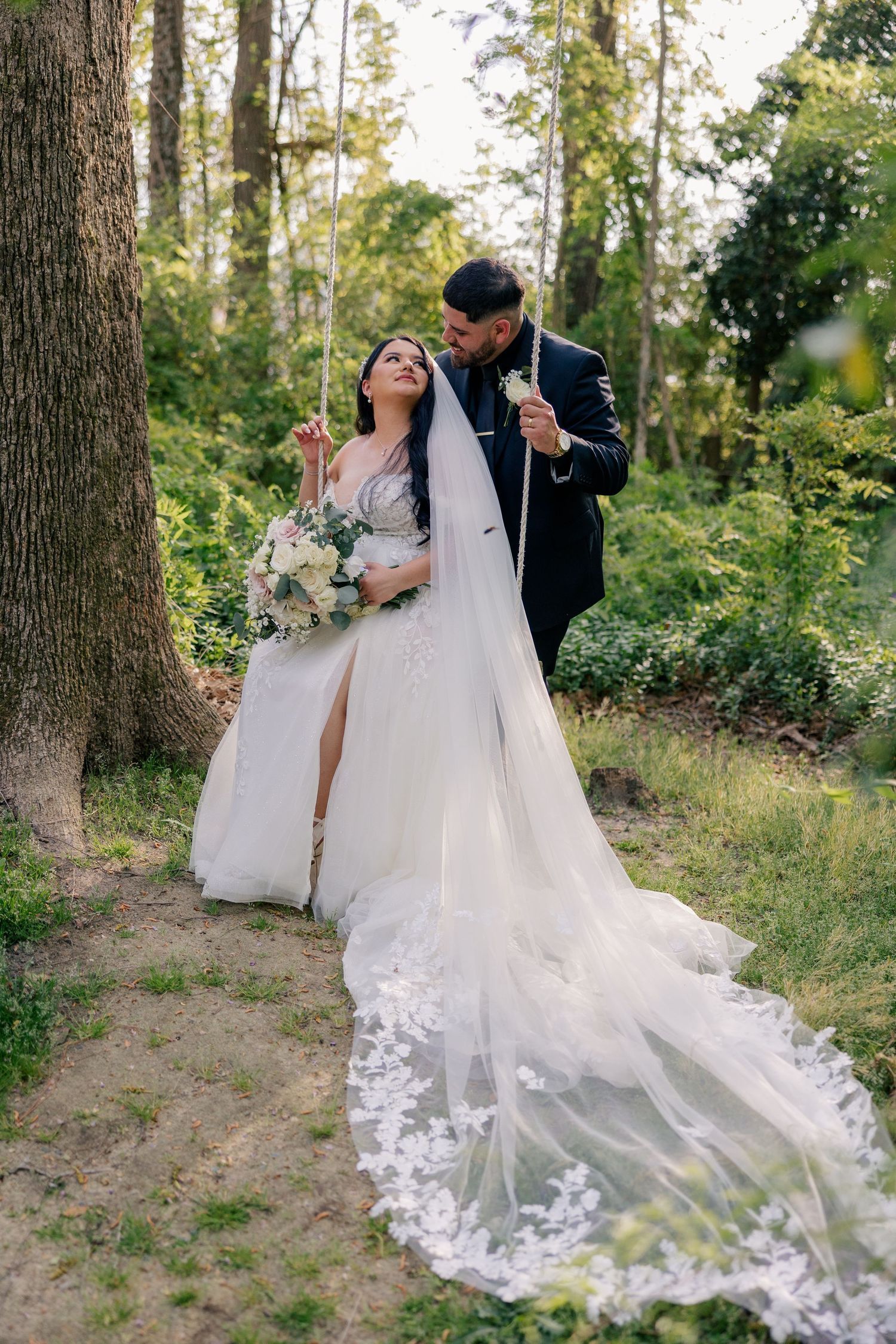 A romantic woodland wedding scene with a flowing lace-trimmed veil trailing behind the couple.