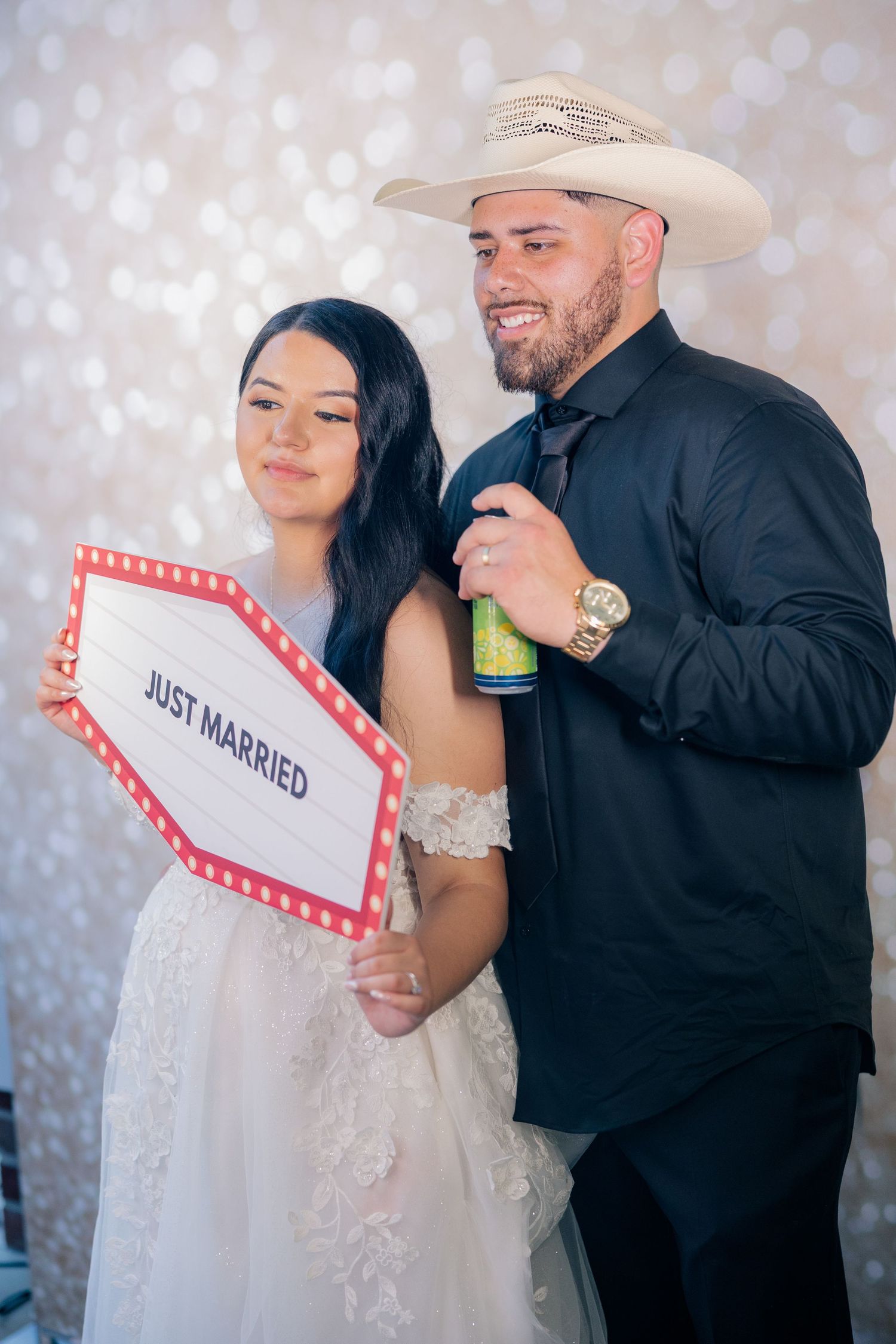 Newlyweds pose with Just Married sign against sparkly backdrop at wedding reception.