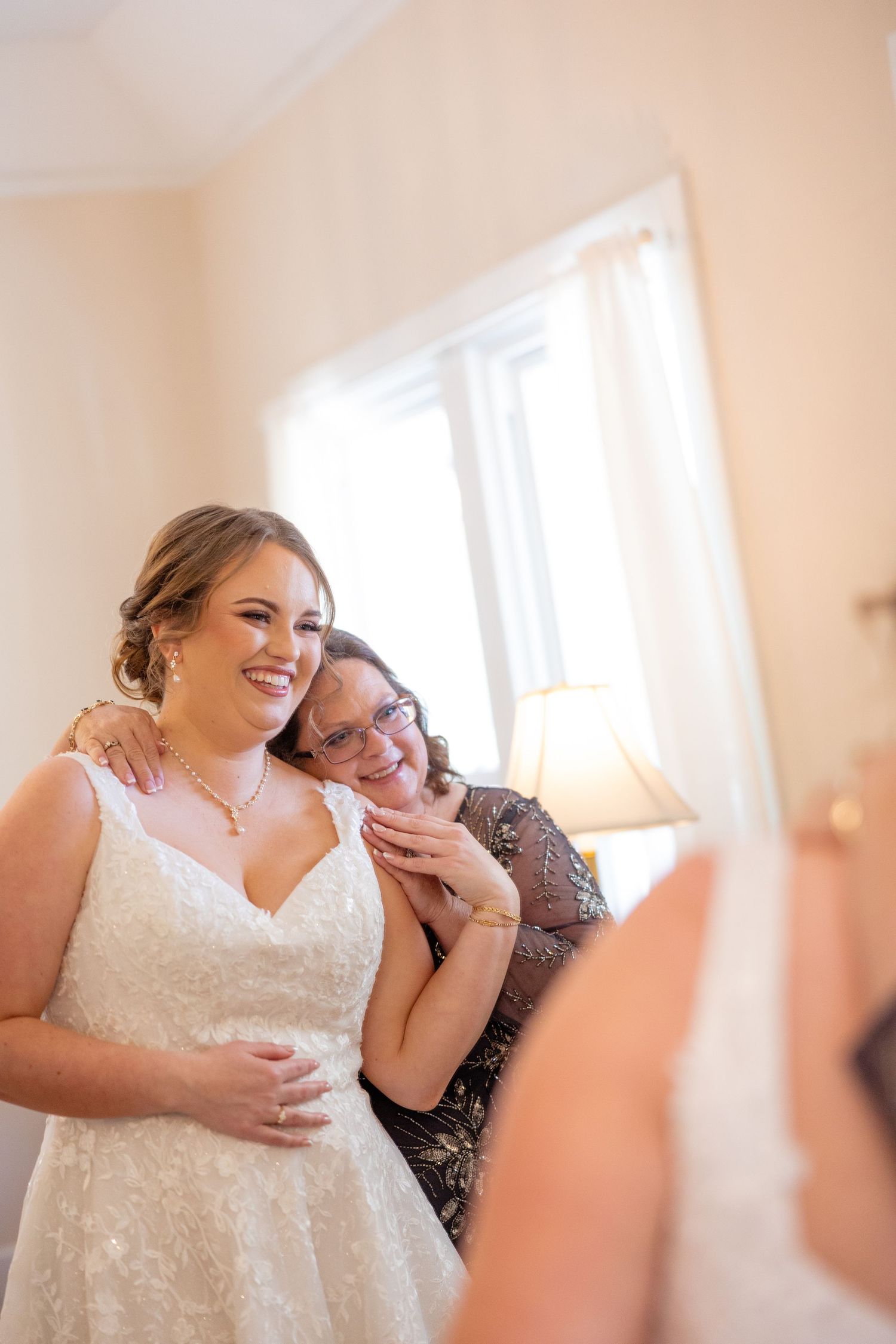 A tender moment of affection between a bride in a lace wedding dress and an older woman during wedding preparations.