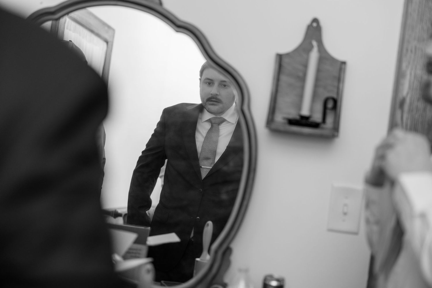 Black and white photo of people preparing in a room with a vintage mirror.