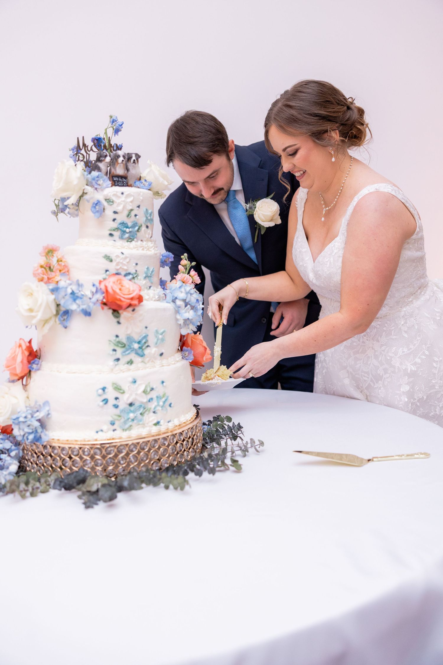 Wedding cake decorated with blue and coral sugar flowers being cut at the reception.