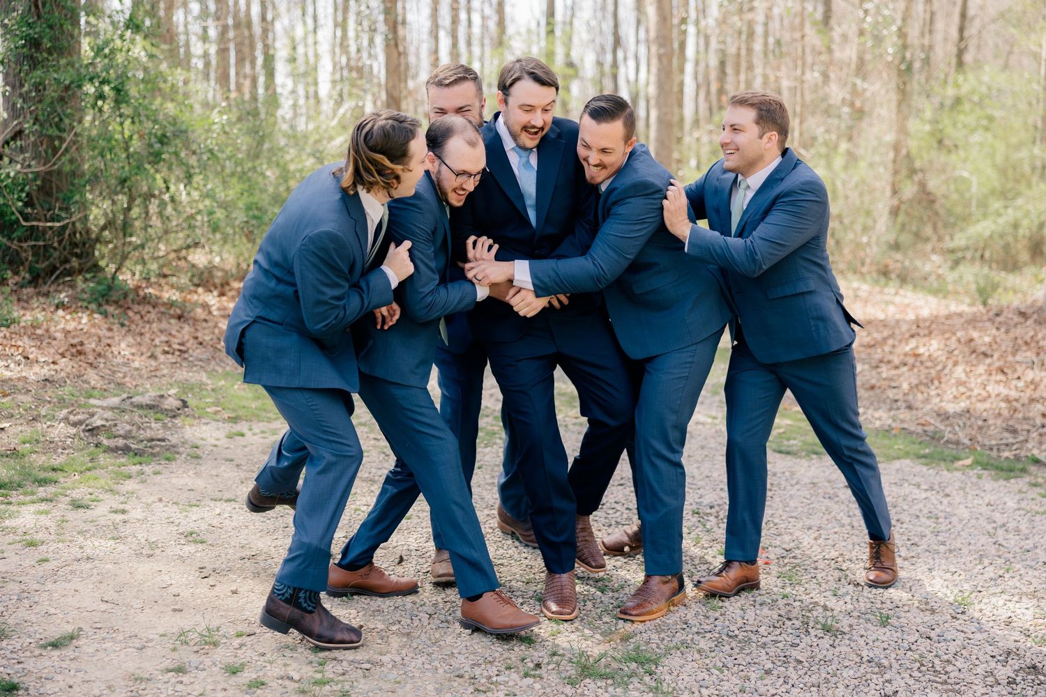 A group of groomsmen in navy suits pose casually on the ground outdoors.