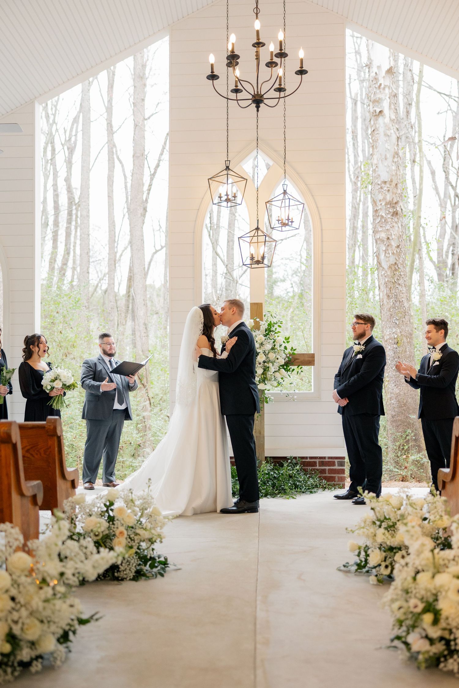 Wedding ceremony in progress at modern white chapel with floral decorations.
