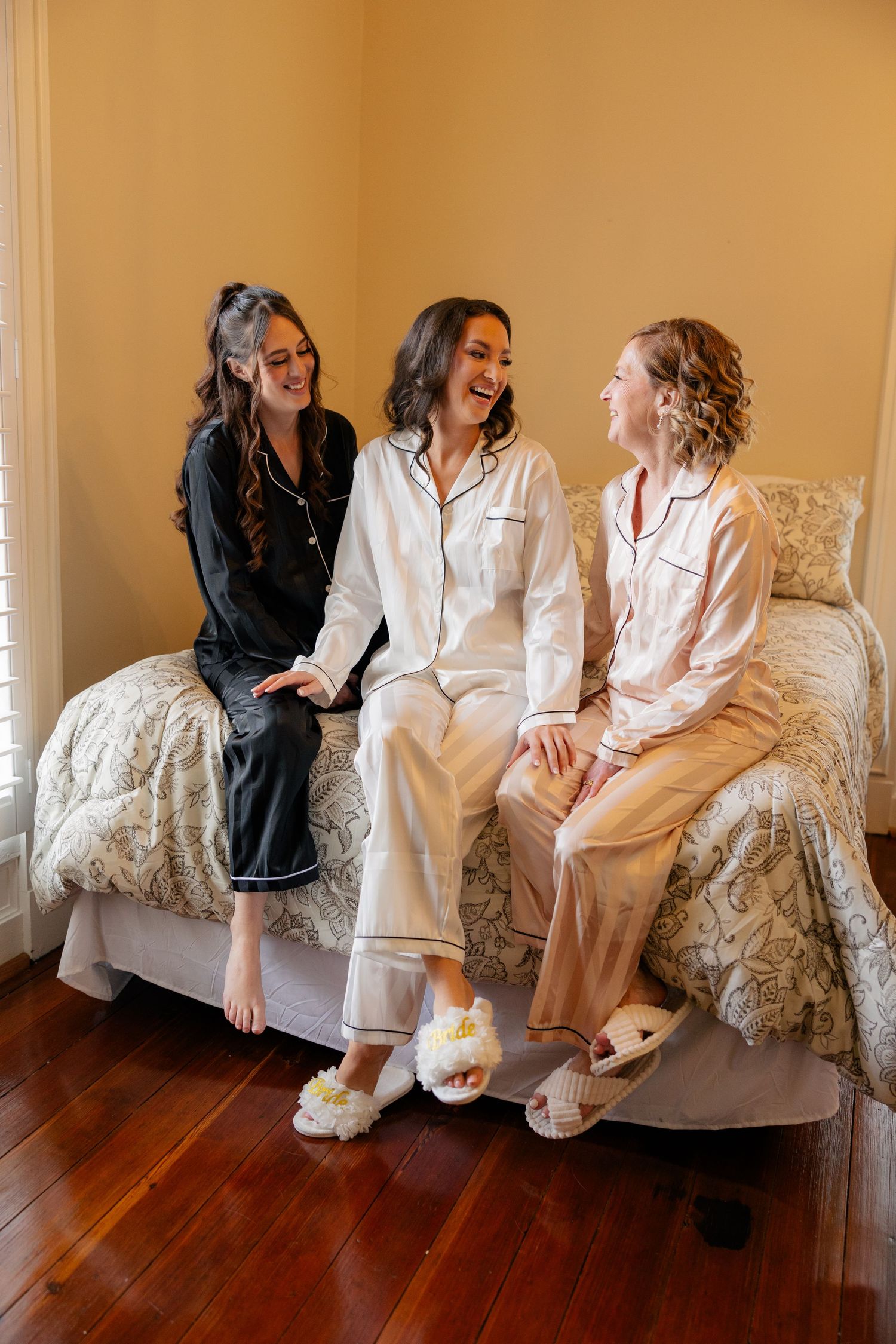 Friends in white robes share joyful moments while sitting on an elegant floral sofa.