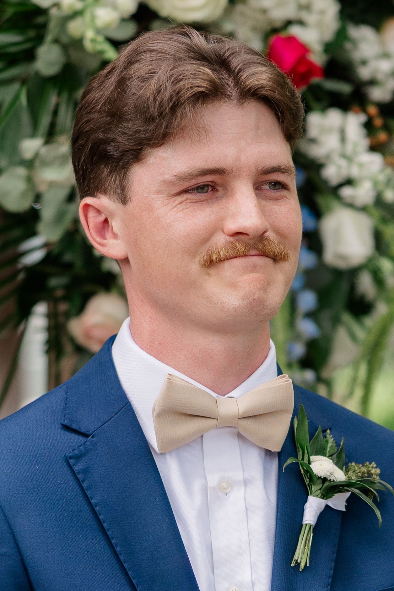 A series of photos showing a person in a navy blue suit and white bowtie with a boutonniere at a formal event.