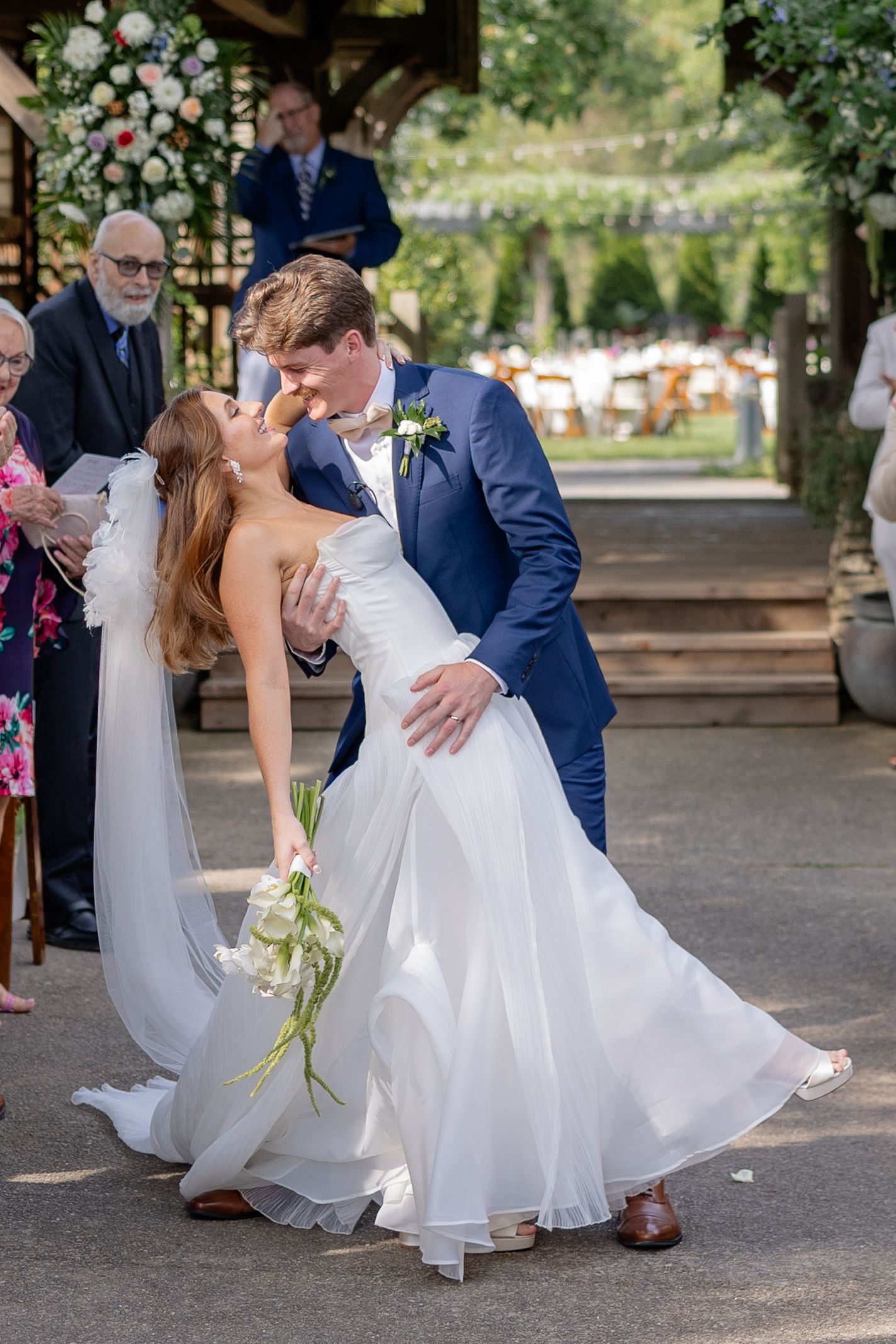 Romantic dip kiss between newlyweds under decorated wedding pavilion.