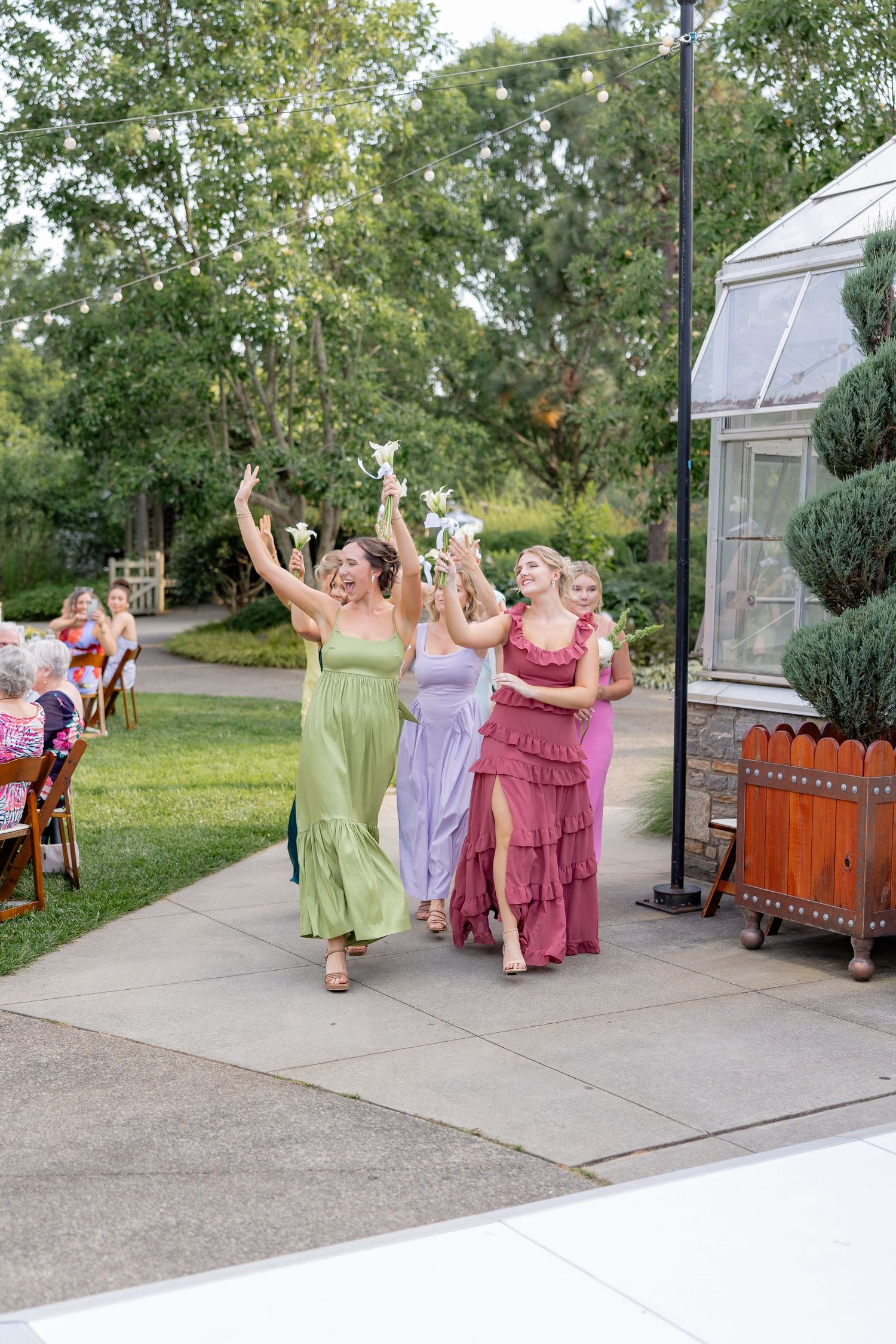 Wedding party in colorful dresses dances and celebrates on an outdoor patio.