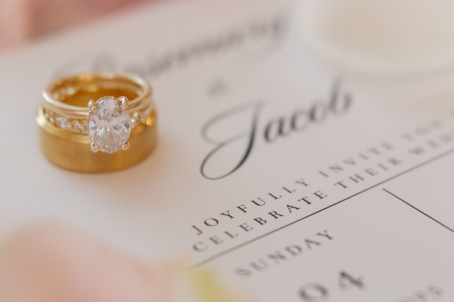 Gold wedding rings and engagement ring rest on white invitation paper with elegant calligraphy text.