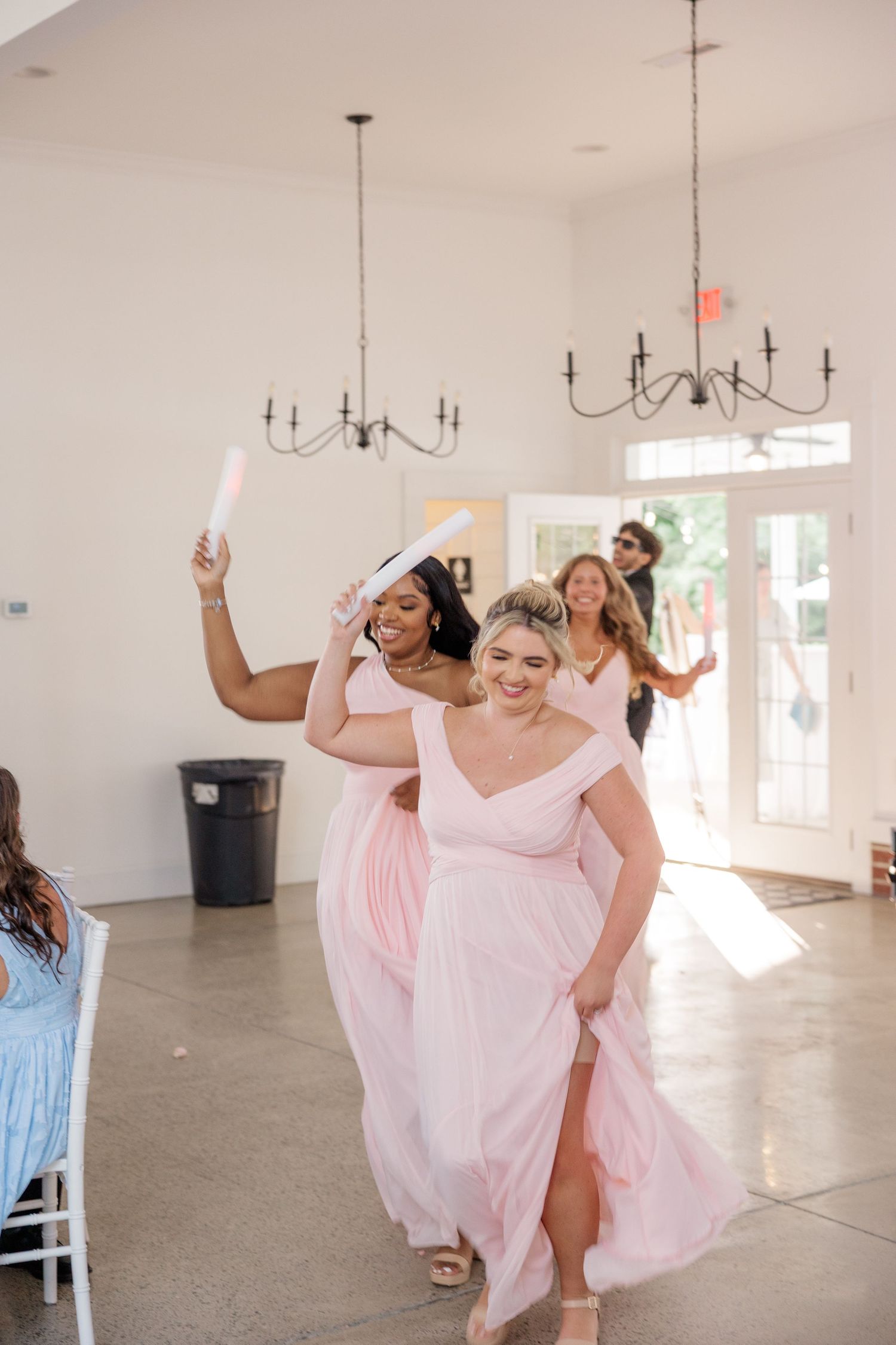 Bridesmaids in pink dresses dancing joyfully in bright reception hall.