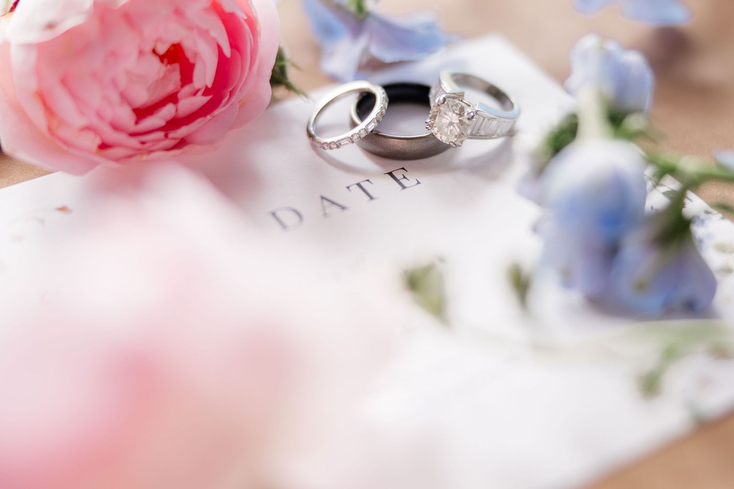Two silver wedding rings rest among soft pink roses and delicate blue flowers in a romantic wedding detail shot.