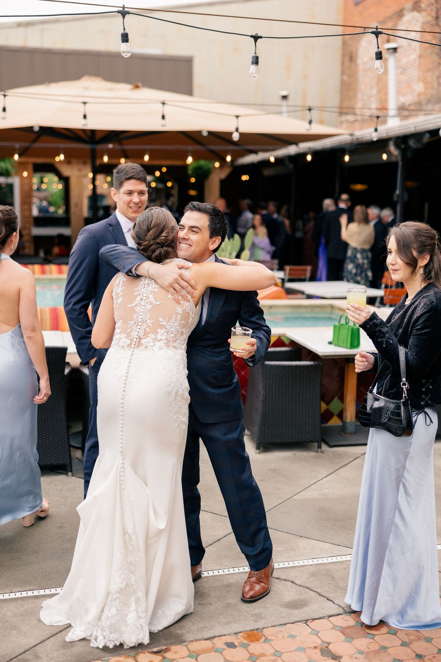 Bride shares a warm hug with a guest during an outdoor wedding cocktail hour celebration.
