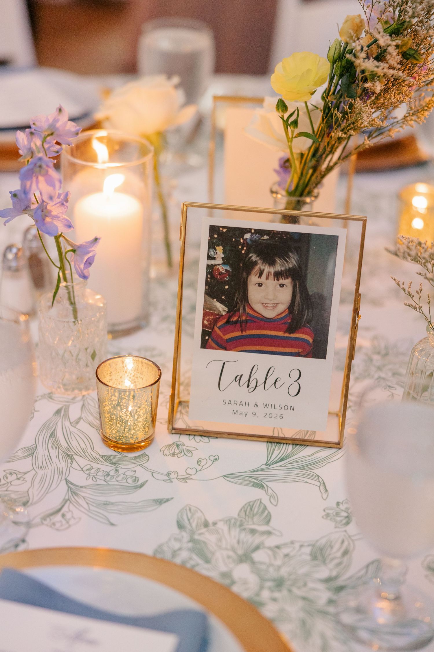 Wedding table centerpiece with childhood photo table number, candles, and wildflower bud vases.