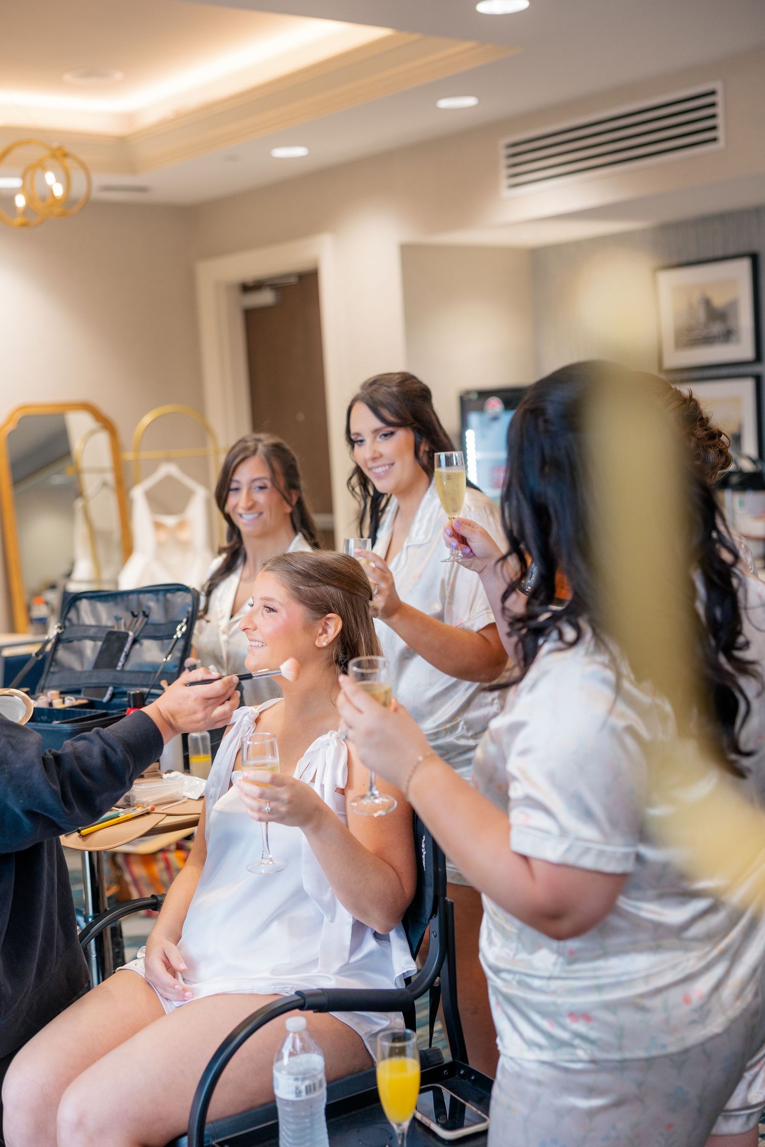 Bridesmaids in white robes toast with champagne glasses while getting ready for a wedding.