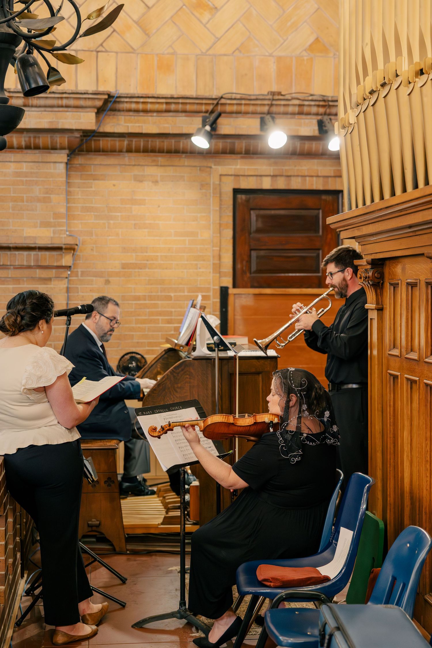 Live wedding ceremony musicians perform with trumpet, violin, and organ in historic brick church venue.