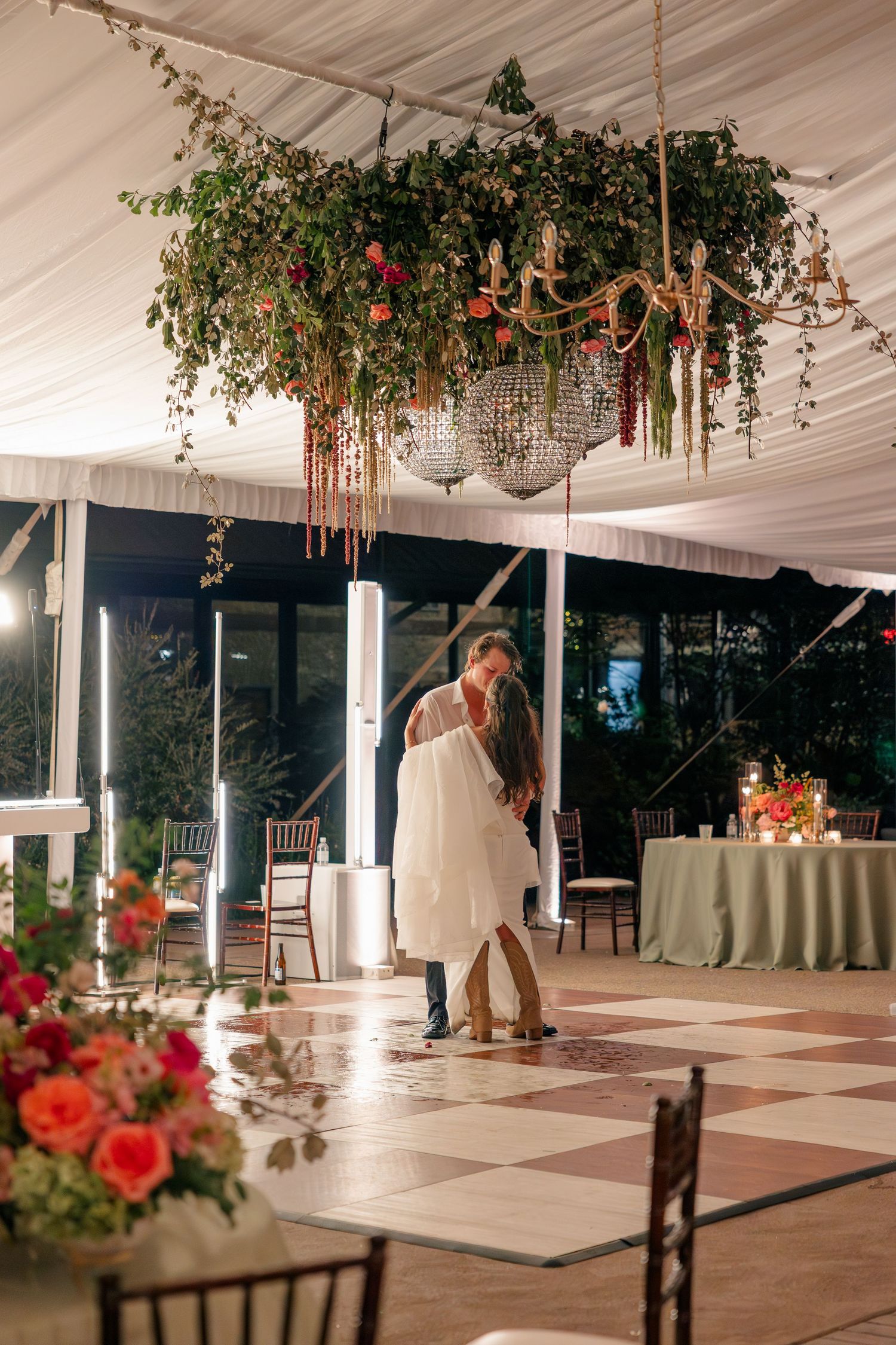 Newlyweds share romantic last dance under a floral chandelier in a softly lit tented wedding venue.