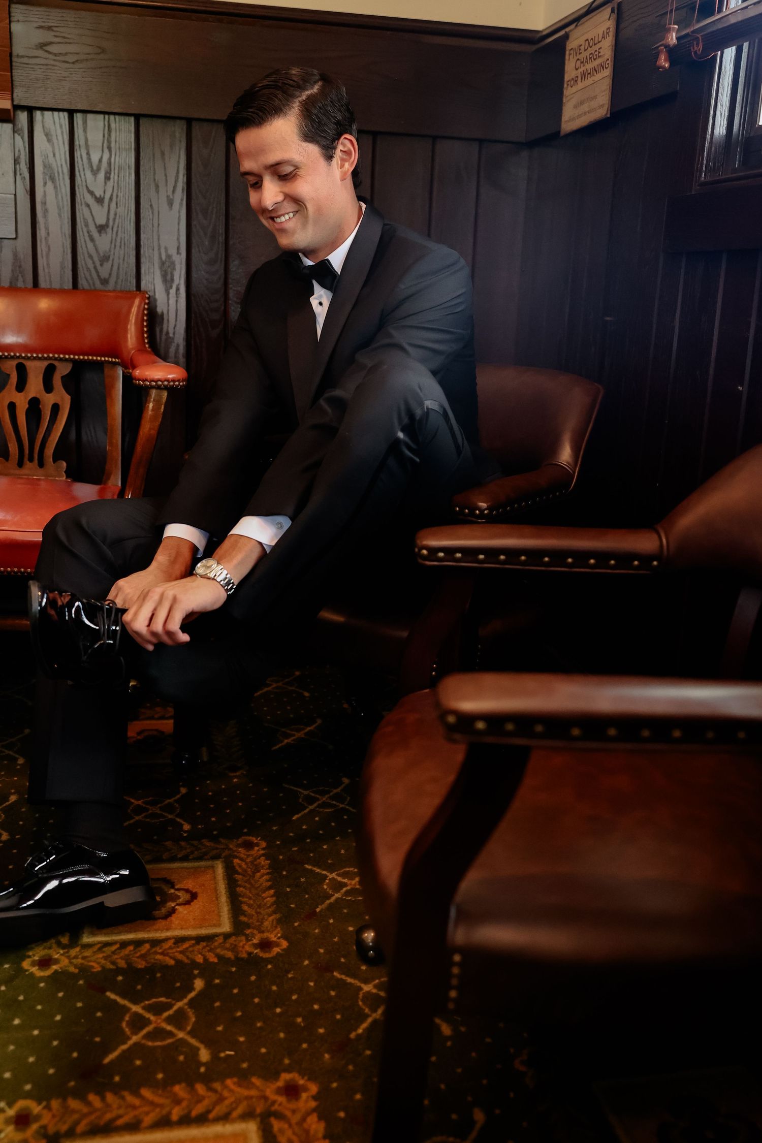 Person in dark suit sitting on leather furniture in dimly lit room with patterned carpet.