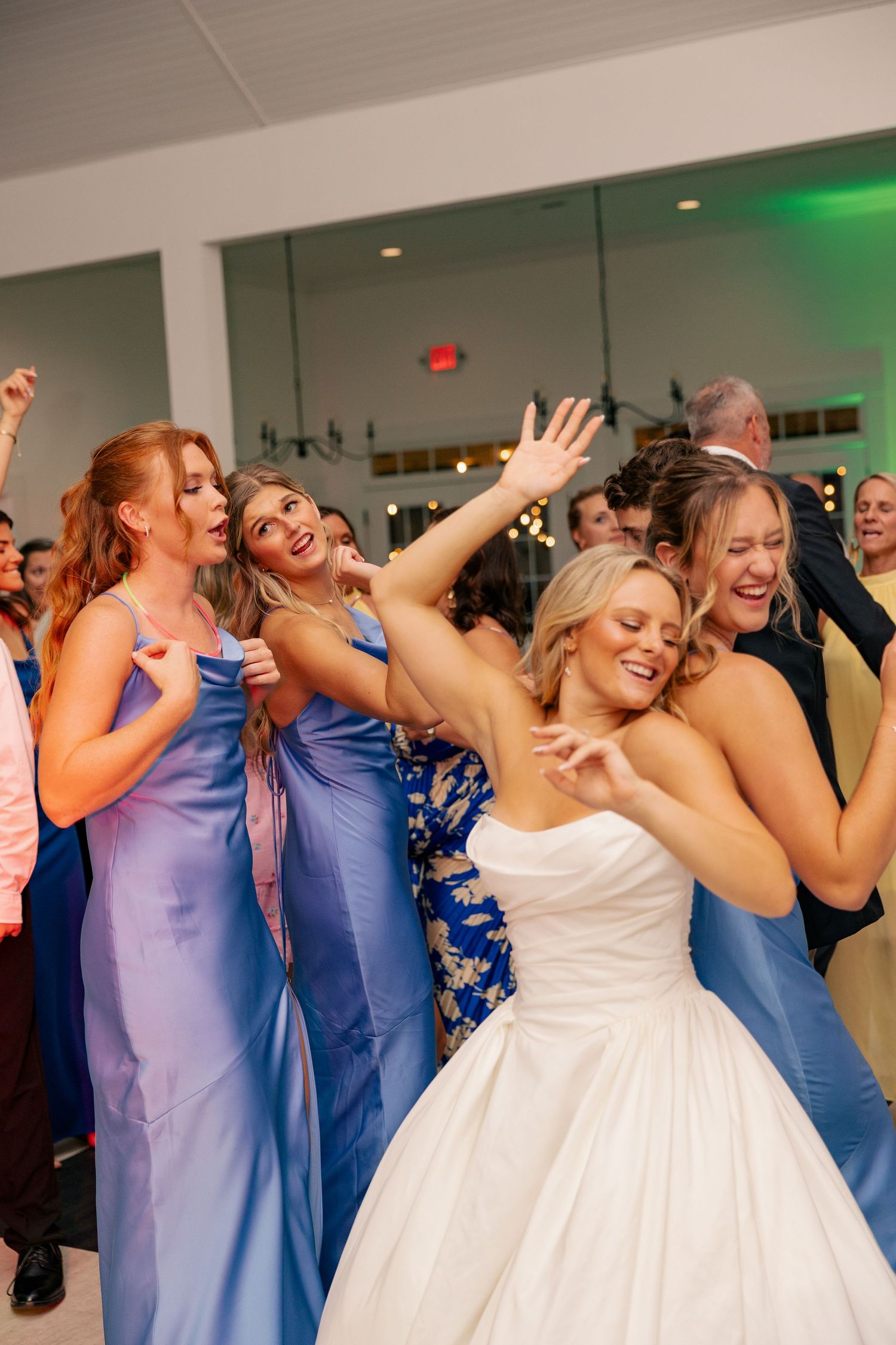 Bride in strapless gown dances joyfully with bridesmaids in blue dresses at wedding reception.