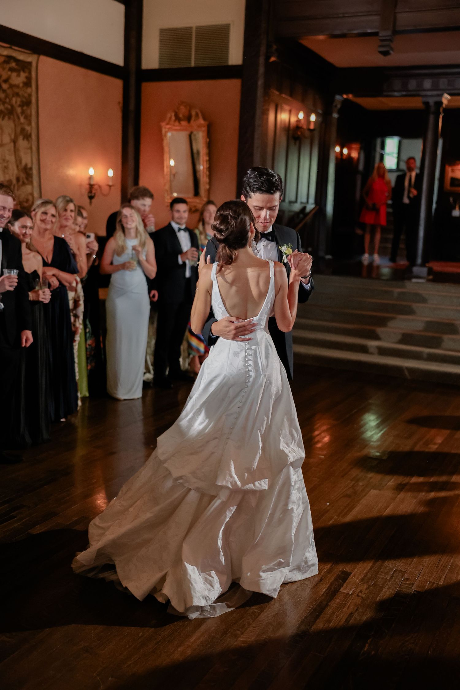 Bride and groom share their first dance at elegant wedding reception while guests watch in formal attire.