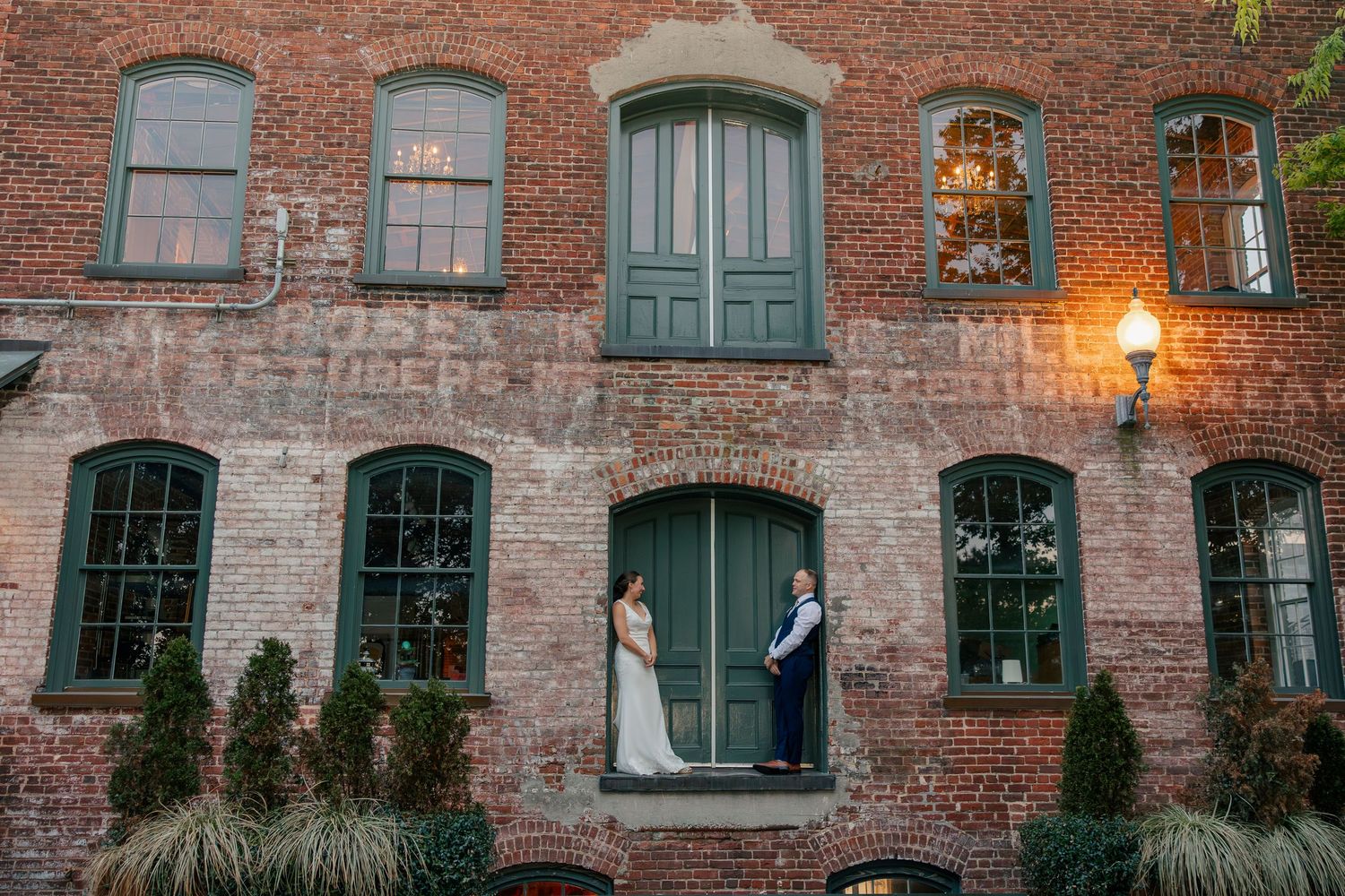 Bride and groom pose romantically in a doorway of a historic brick building at dusk.
