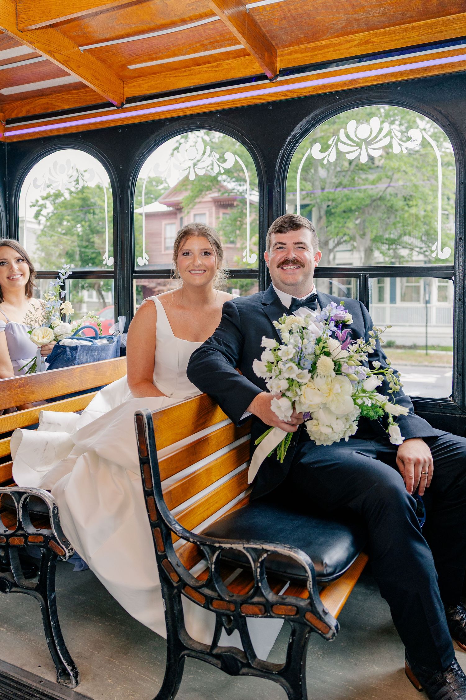 Bride and groom sitting together on vintage trolley holding floral bouquet.