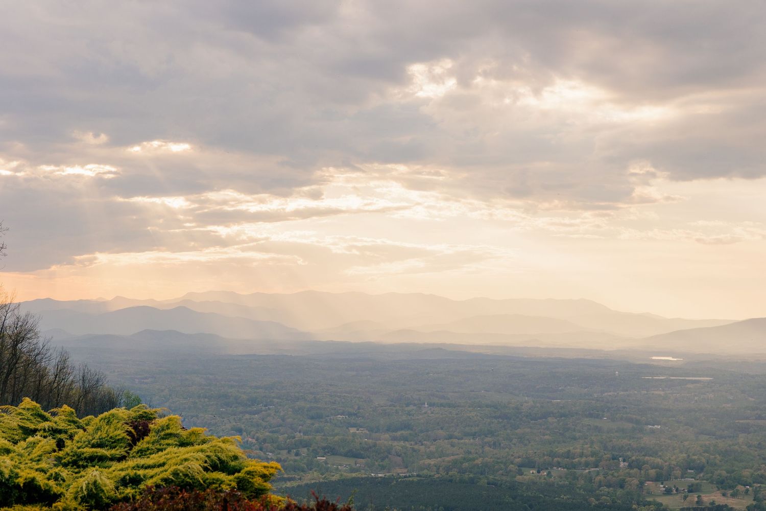 Breathtaking panoramic mountain valley view at sunset with dramatic clouds and golden light over rolling hills.