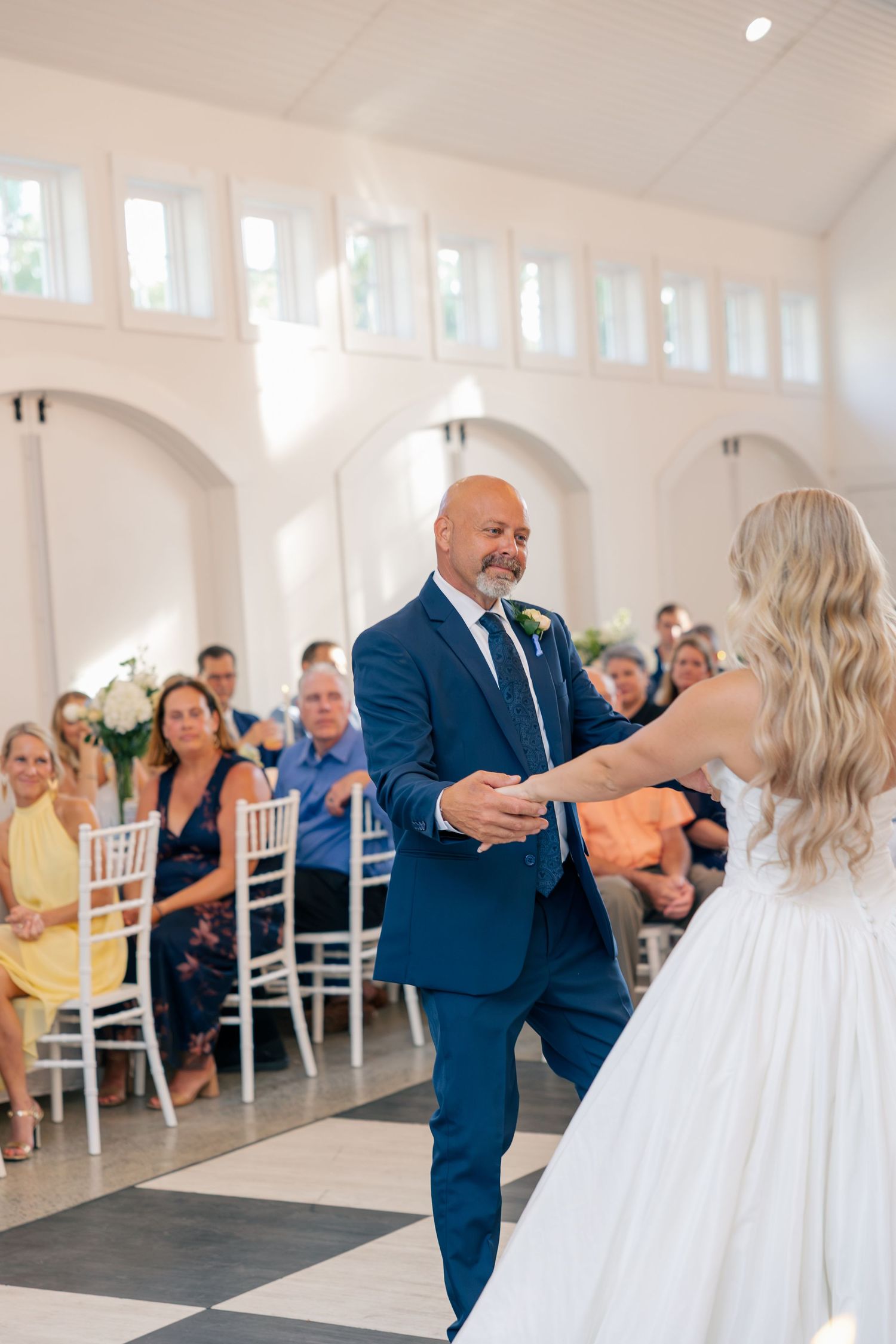 Father of the bride in a navy suit shares a first dance with his daughter in a white ballgown.