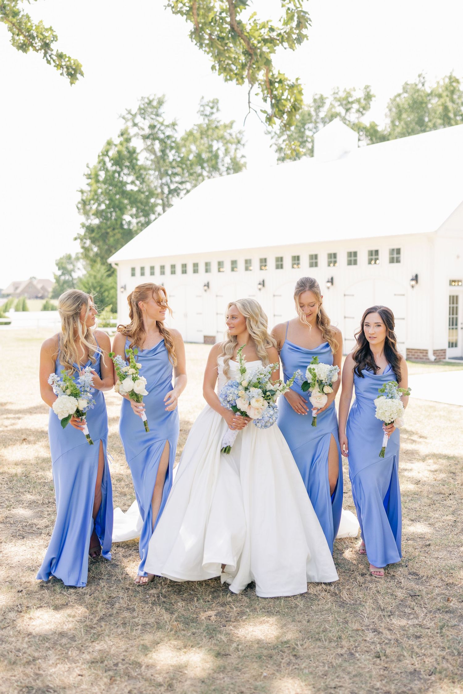 Bride poses with four bridesmaids wearing periwinkle blue gowns holding white bouquets.