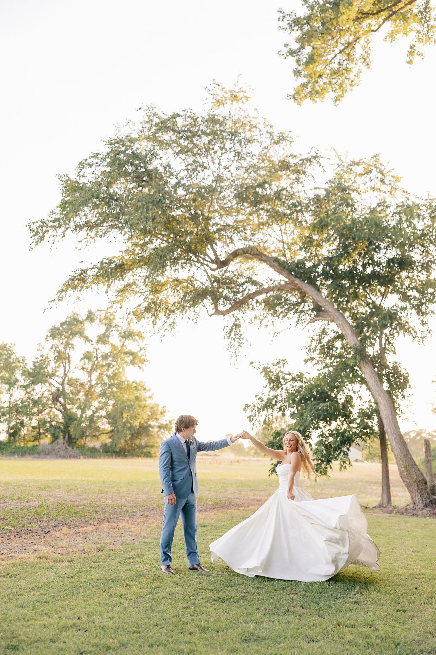 Bride and groom dancing under a large tree at golden hour on a lush green lawn.