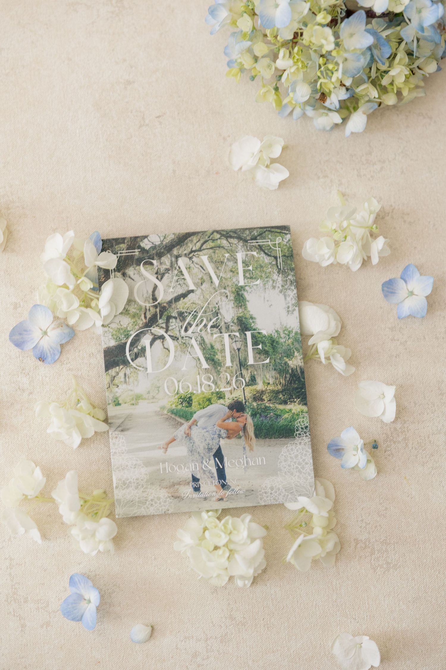 Elegant save the date card surrounded by blue and white hydrangea petals on a neutral background.
