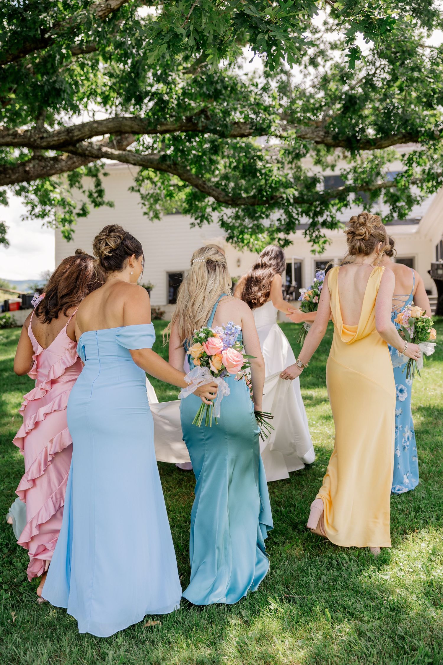 Bridesmaids in pastel dresses walking together on green grass during a summer wedding.